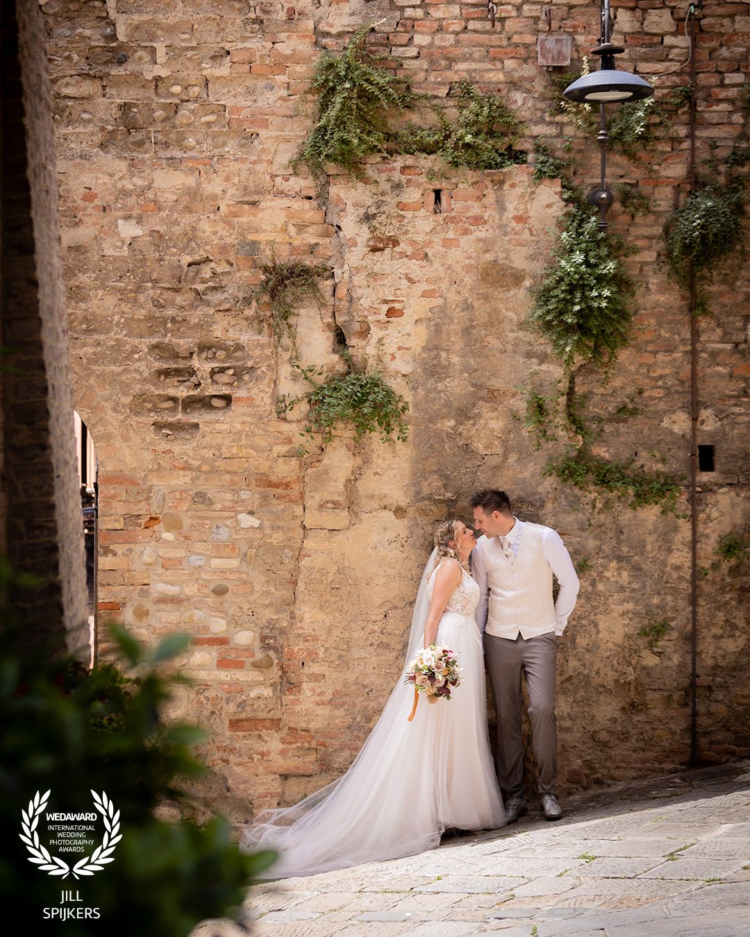 Wedding photography along a rustic brick wall with climbing vines and natural lighting.