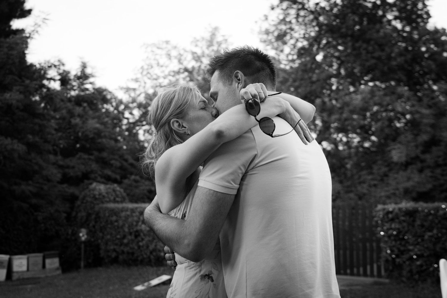 Couple sharing romantic kiss outdoors in garden setting captured in black and white photography.
