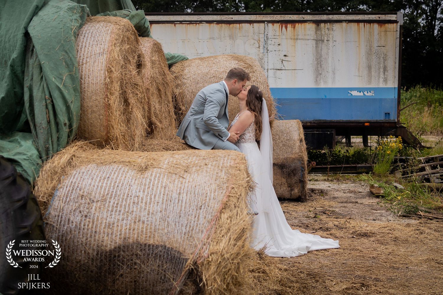 Romantic countryside portrait with couple on hay bales near rustic barn.