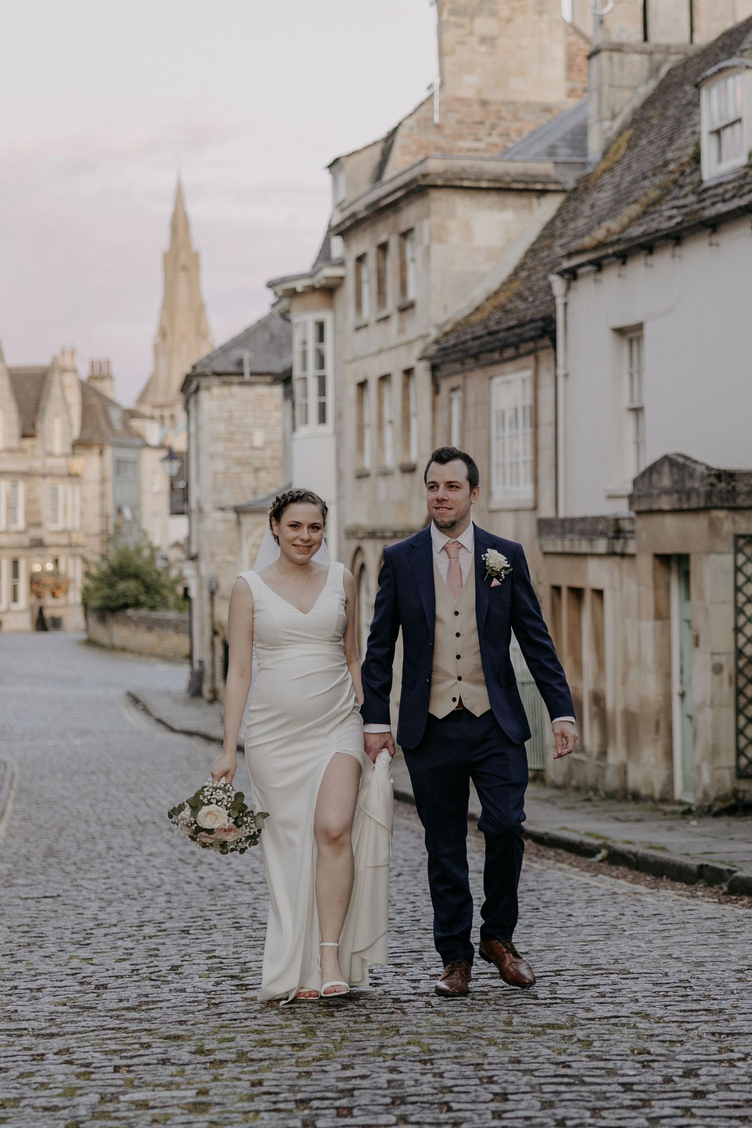 Newlyweds walking along a historic cobblestone street with classic architecture.