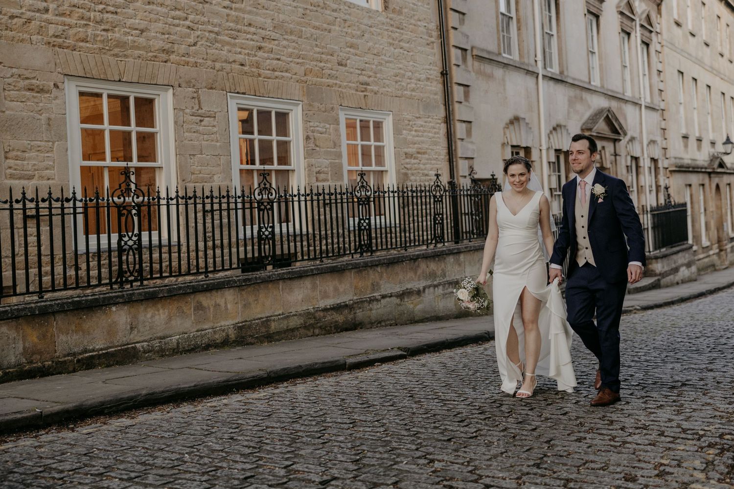 Wedding couple strolling down a charming Edinburgh street lined with historic stone buildings.