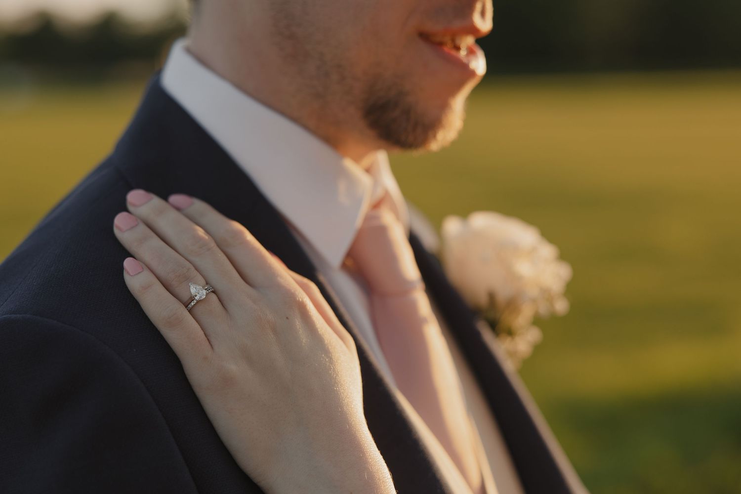 Close-up of a hand wearing a wedding ring resting on formal attire during sunset.