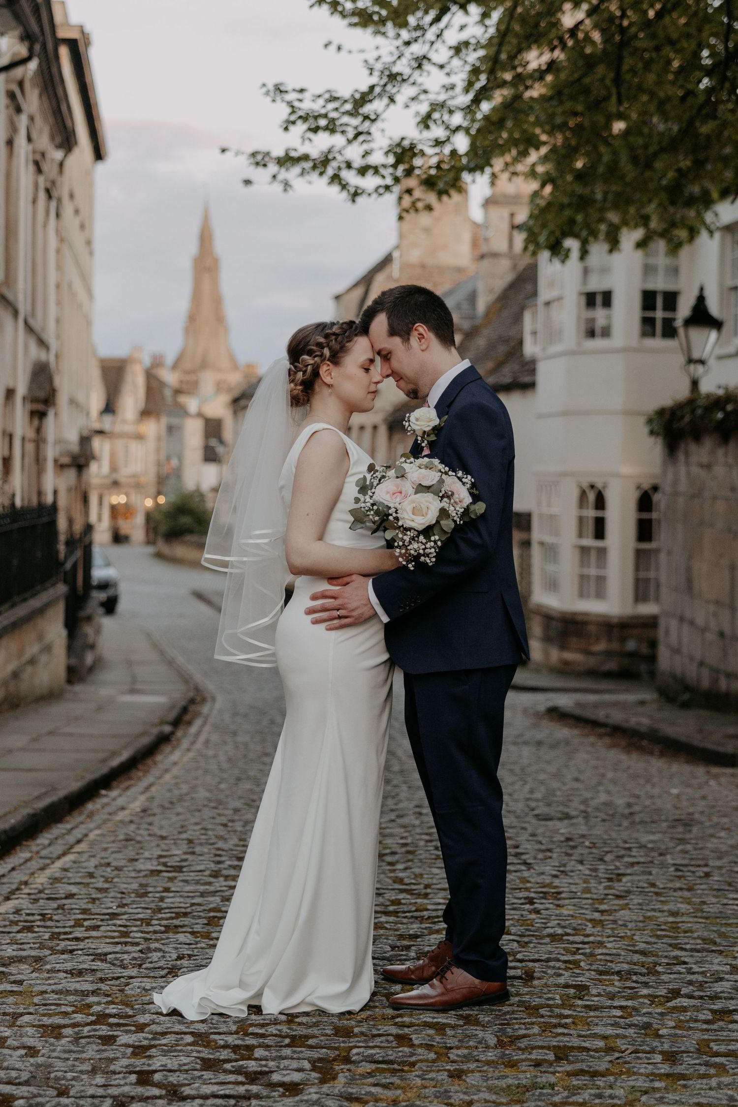A romantic wedding moment on a charming European street with a church spire in the background.