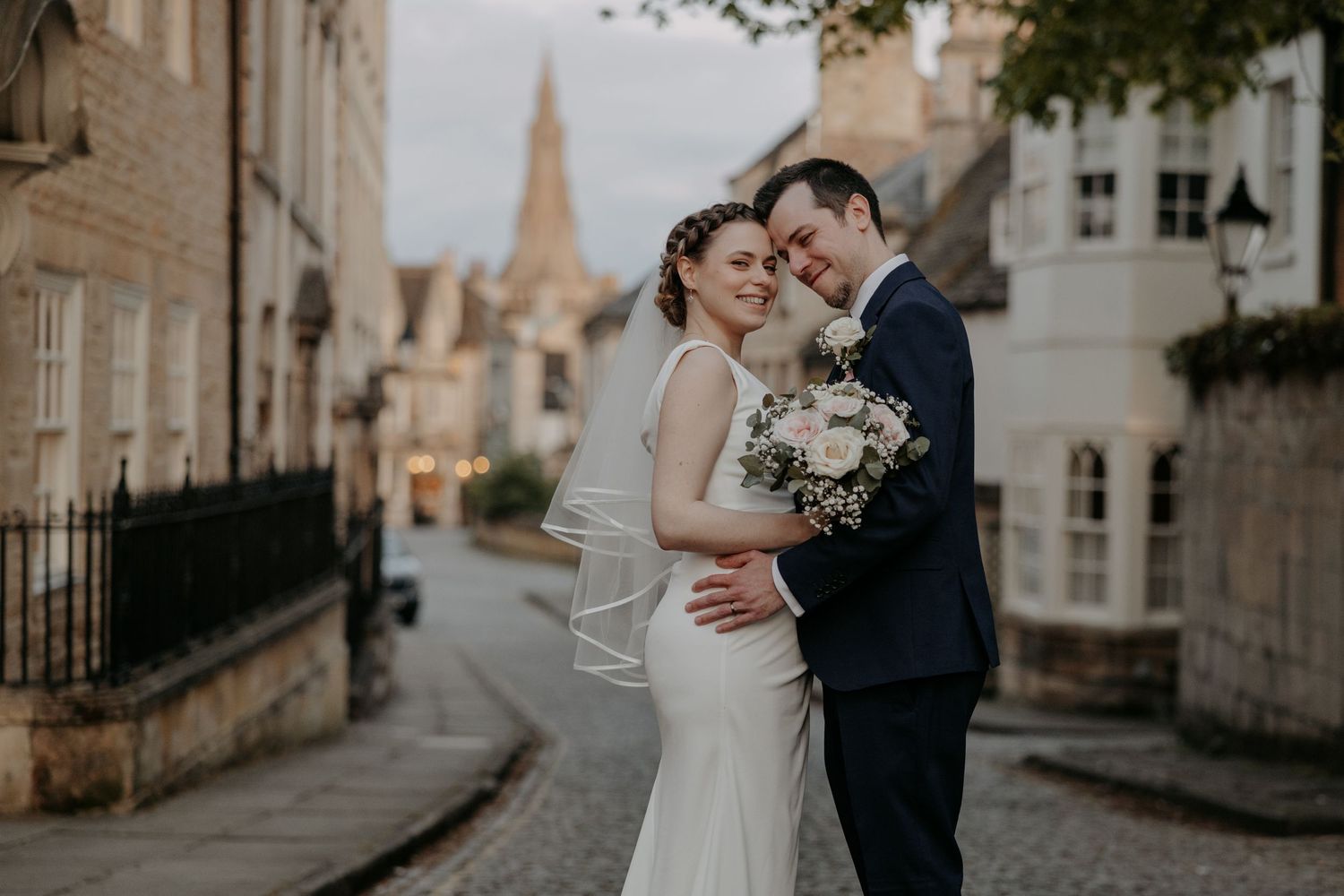 A romantic embrace between newlyweds on a quaint cobblestone street with historic architecture.