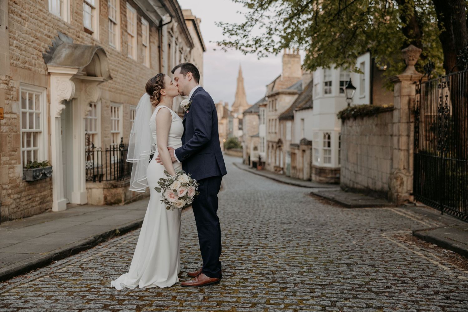 Newlyweds share a tender moment on a historic cobblestone street with stone buildings.