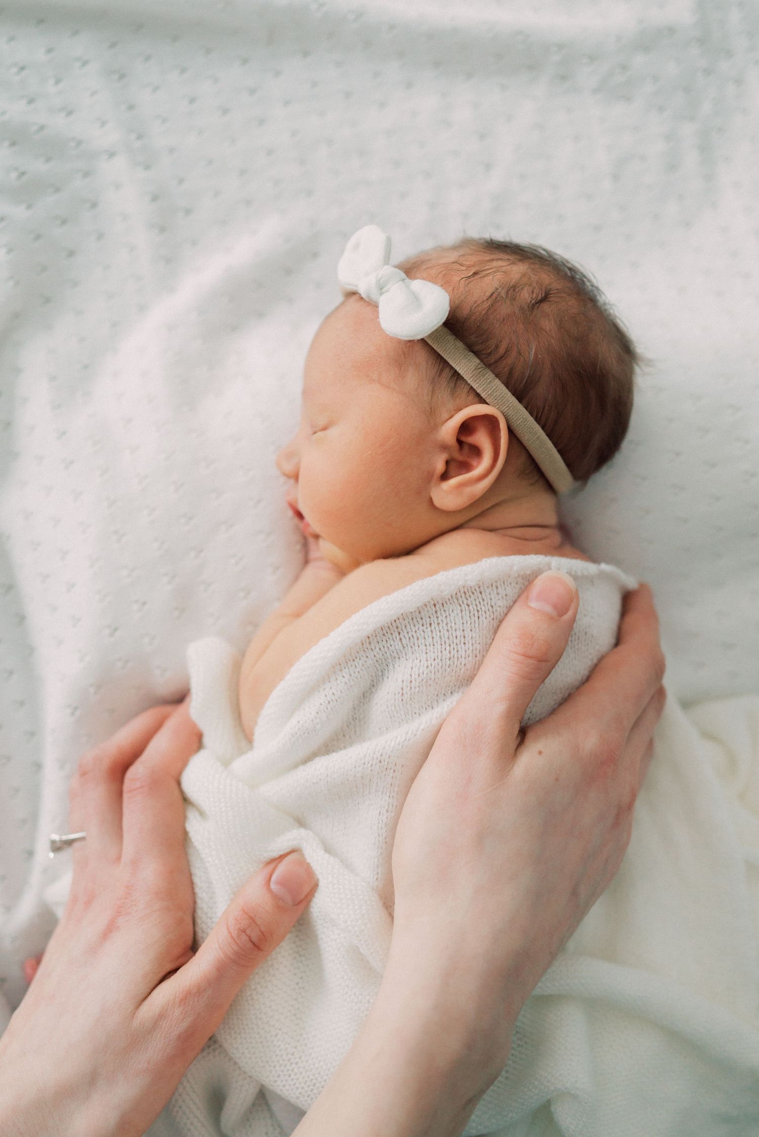 Gentle hands cradle sleeping newborn wearing delicate bow headband.