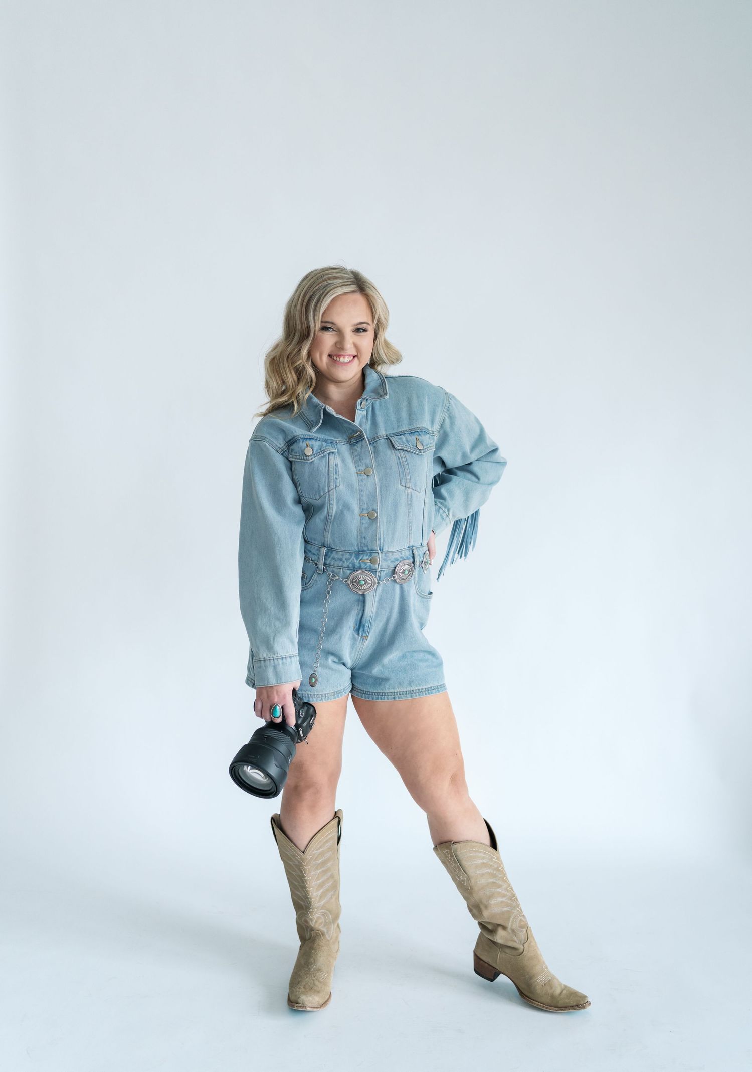 A distressed denim jacket worn with cowboy boots in a studio setting against a white background.