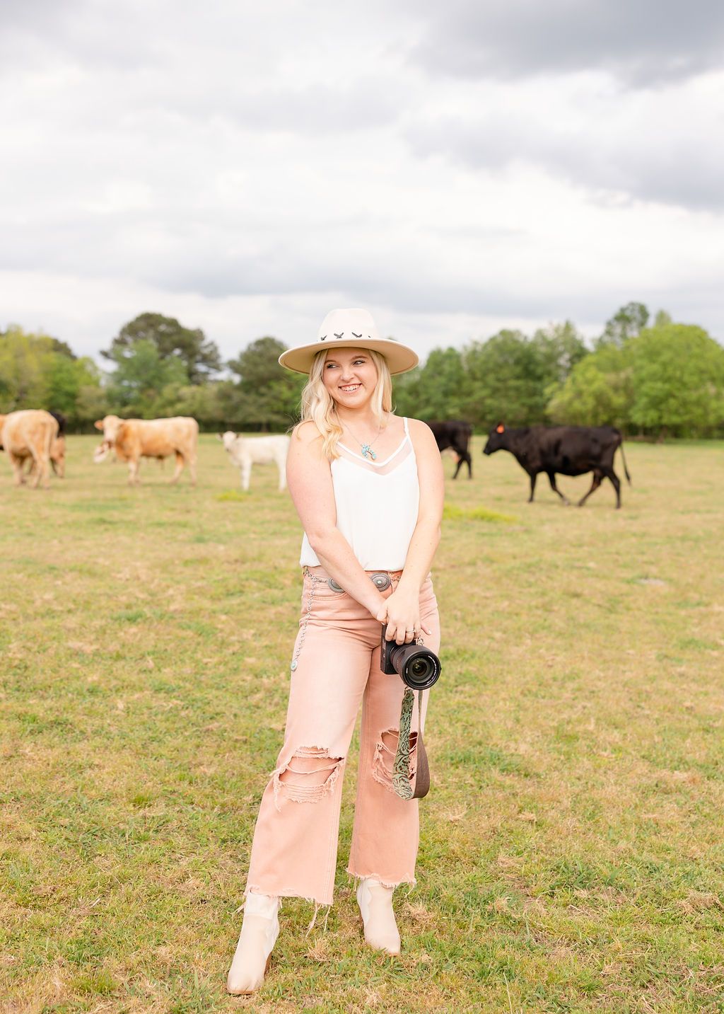 Cattle graze on a grassy pasture under cloudy skies while someone in a straw hat walks through the field.