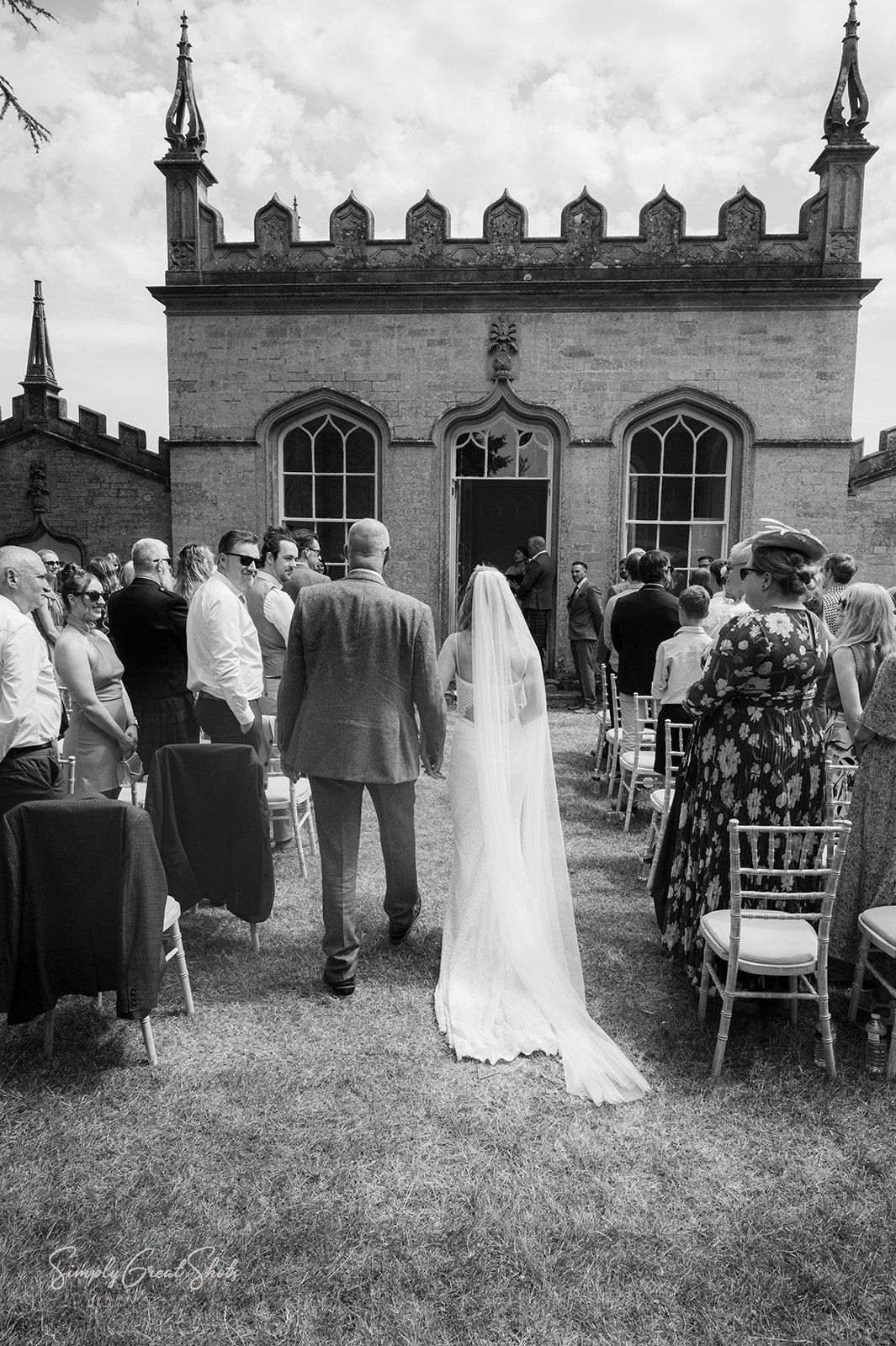 A black-and-white photograph of a wedding ceremony taking place outdoors next to the Gothic-style building at Fort Henry.