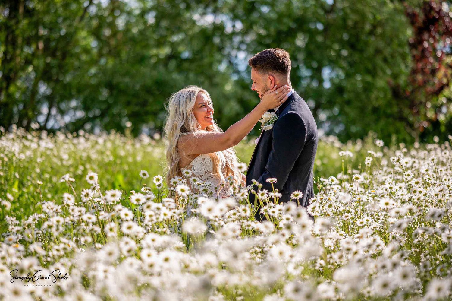 A couple stand close together in a beautiful meadow filled with blooming white daisies on a sunny day at Blackwell Grange Wedding Venue.