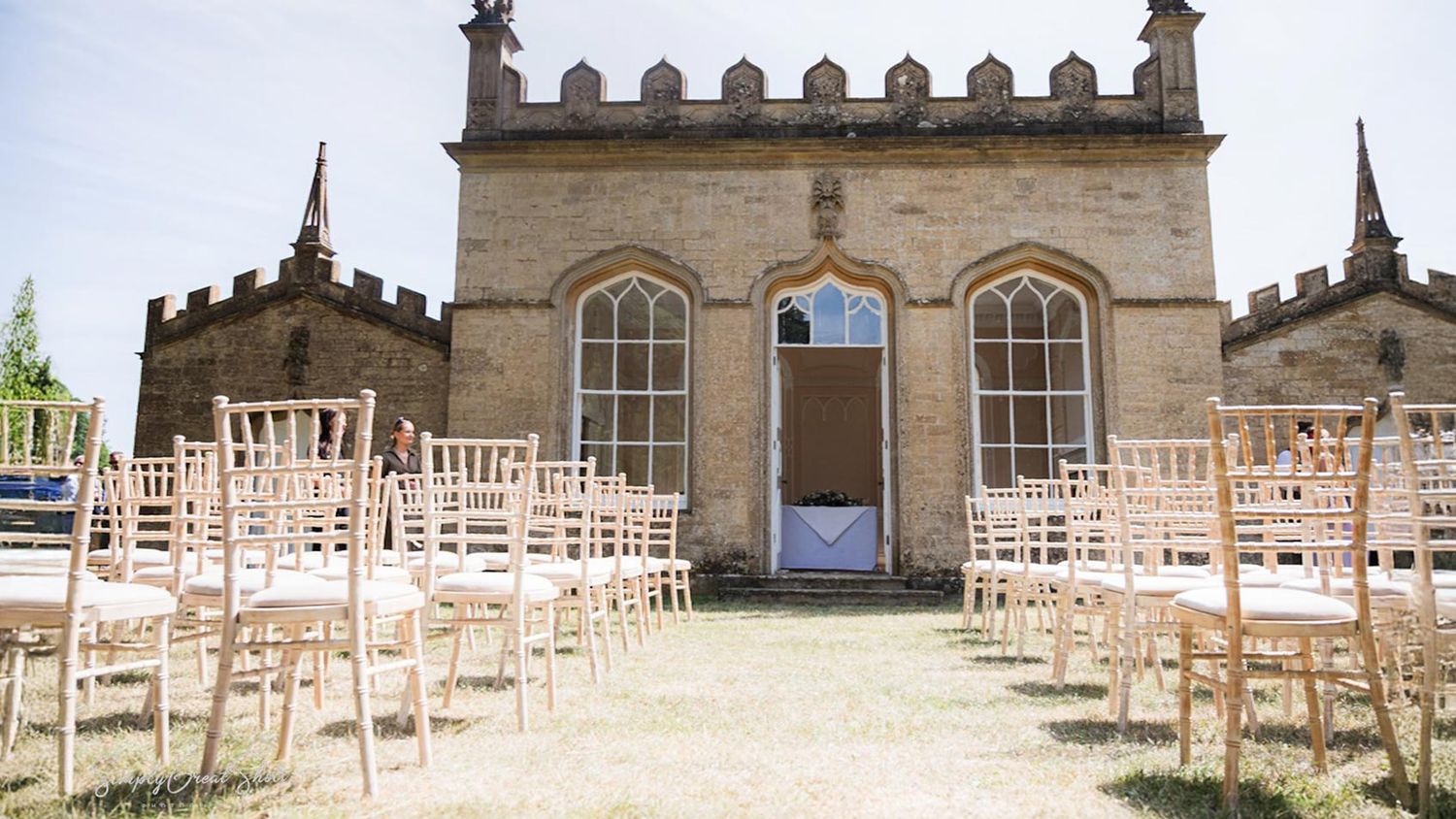 Wooden chairs arranged in rows for a wedding ceremony outside Fort Henry, a Gothic-style stone chapel with arched windows.