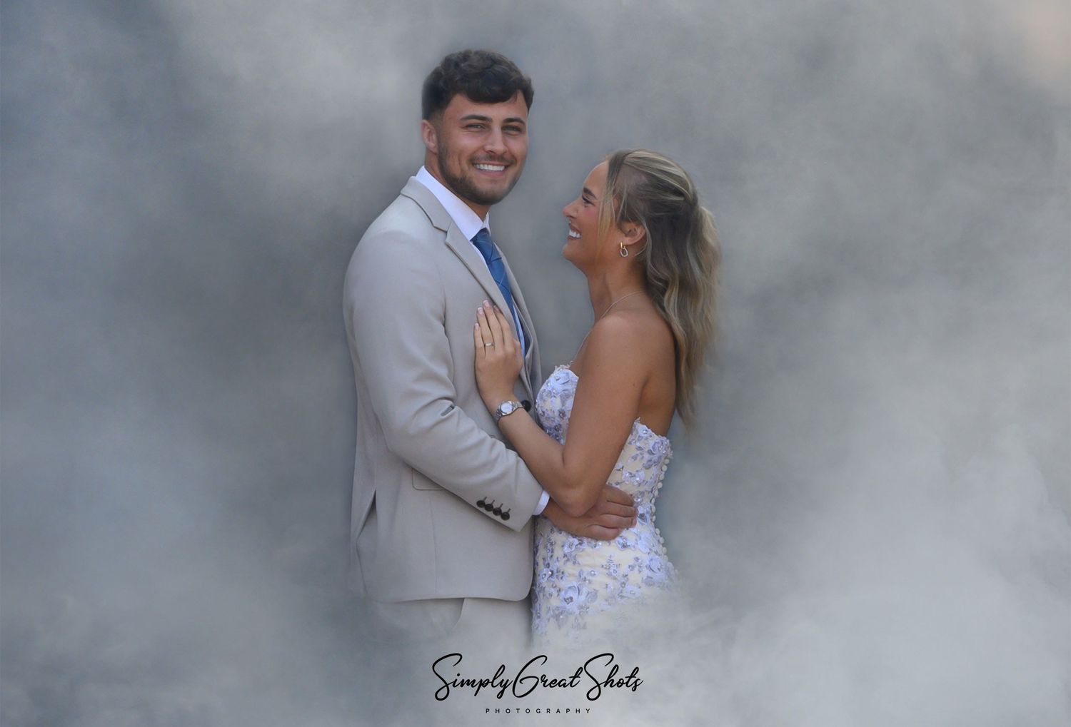 A wedding couple embrace and laugh together surrounded by the smoke from a white smoke bomb during their wedding day photo session.