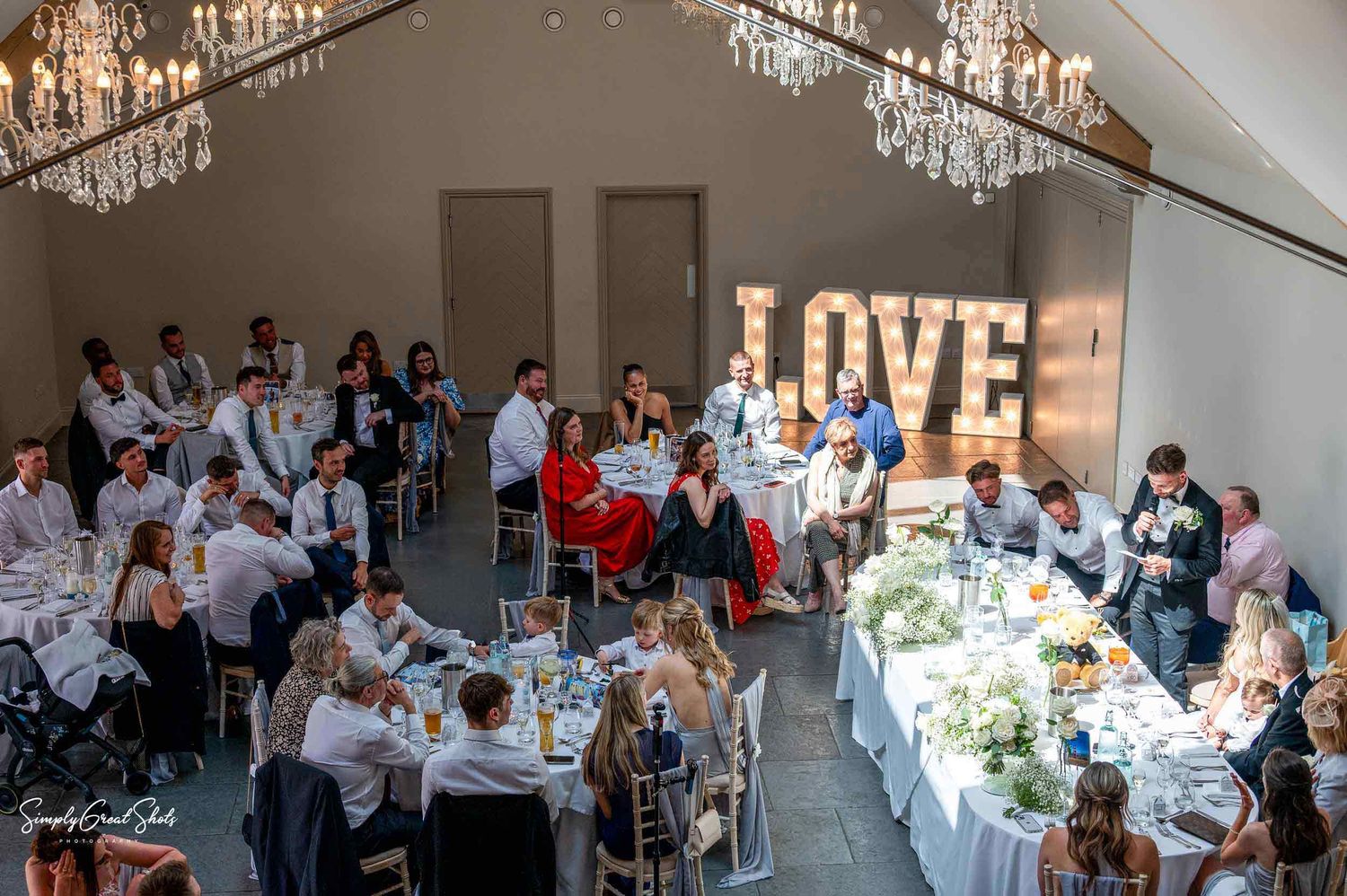 At the Blackwell Grange wedding reception, guests are seated at dining tables beneath crystal chandeliers with an illuminated LOVE sign.