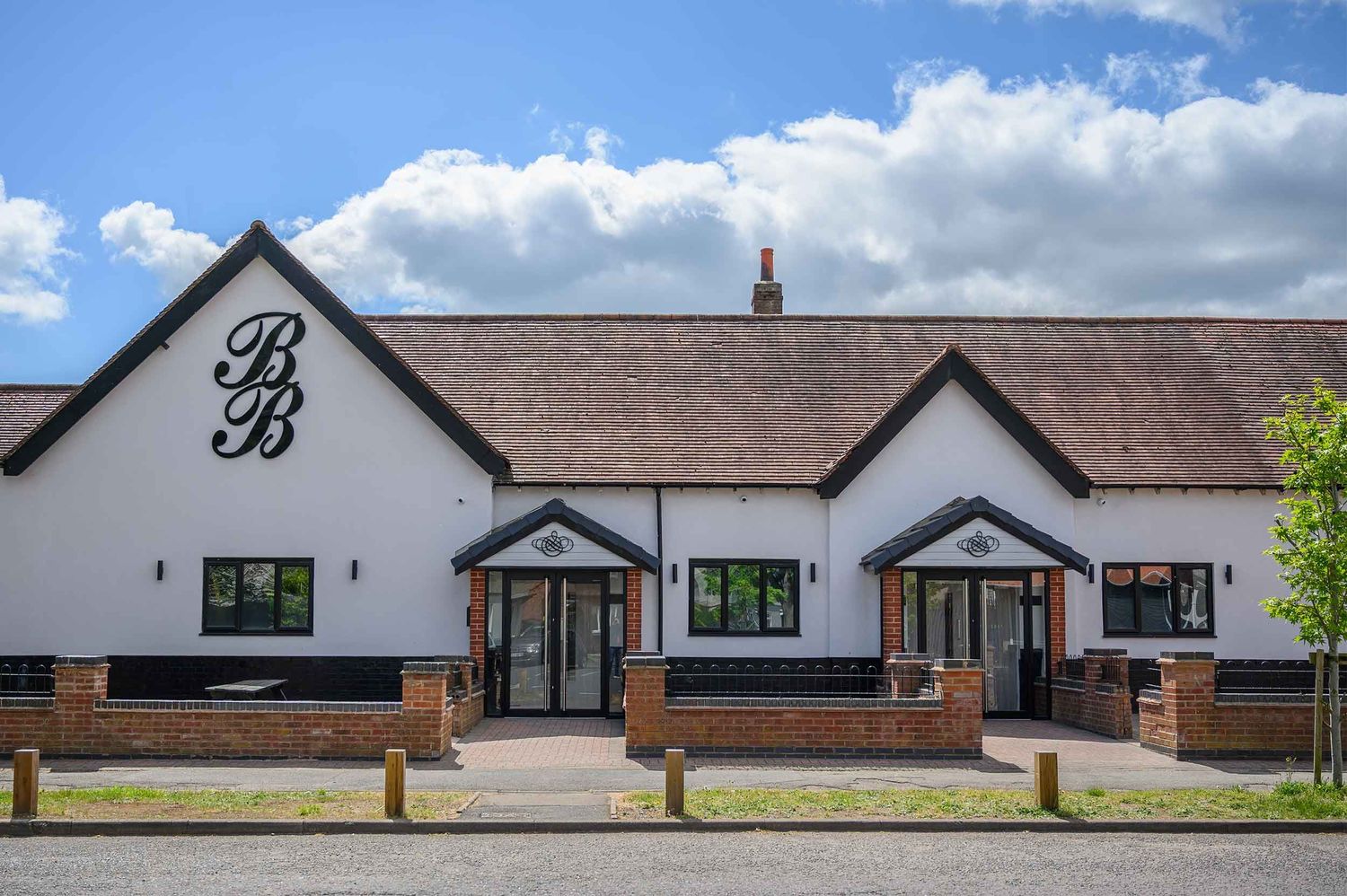 Binley Banqueting Suite, Coventry, features two entrance doors and decorative BB lettering under a brown roof against a blue sky.