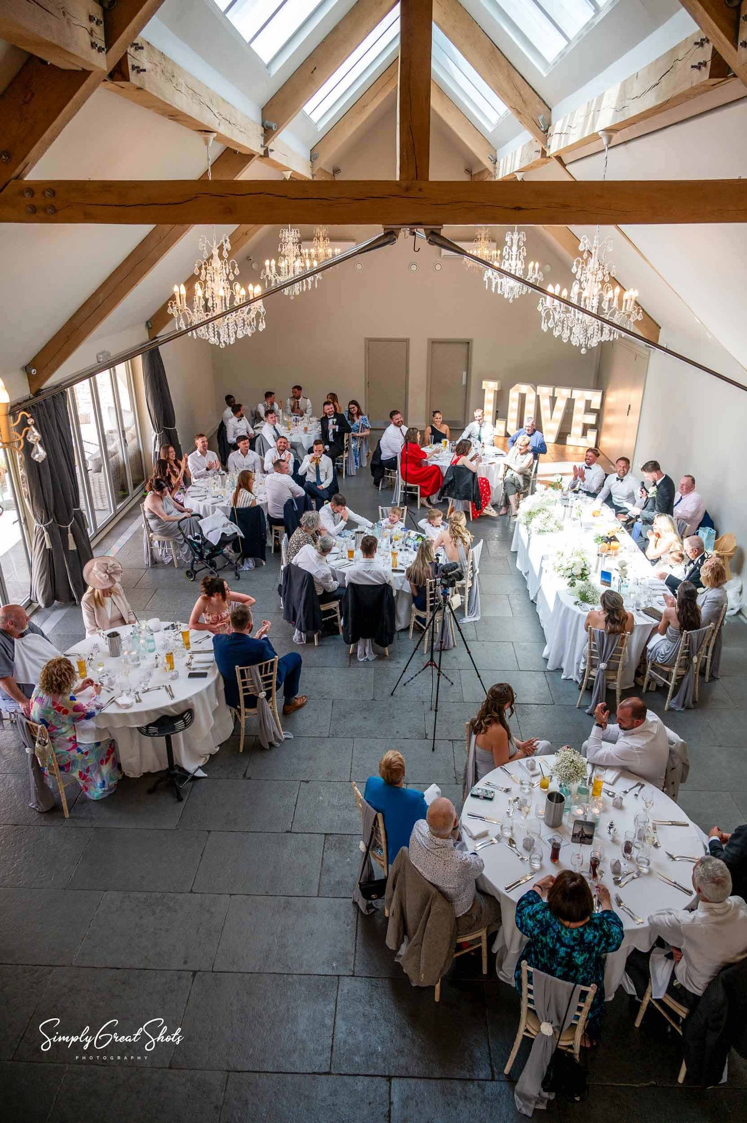 Blackwell Grange wedding reception guests seated at elegant white tables under rustic wooden beams with skylights in a bright venue space.