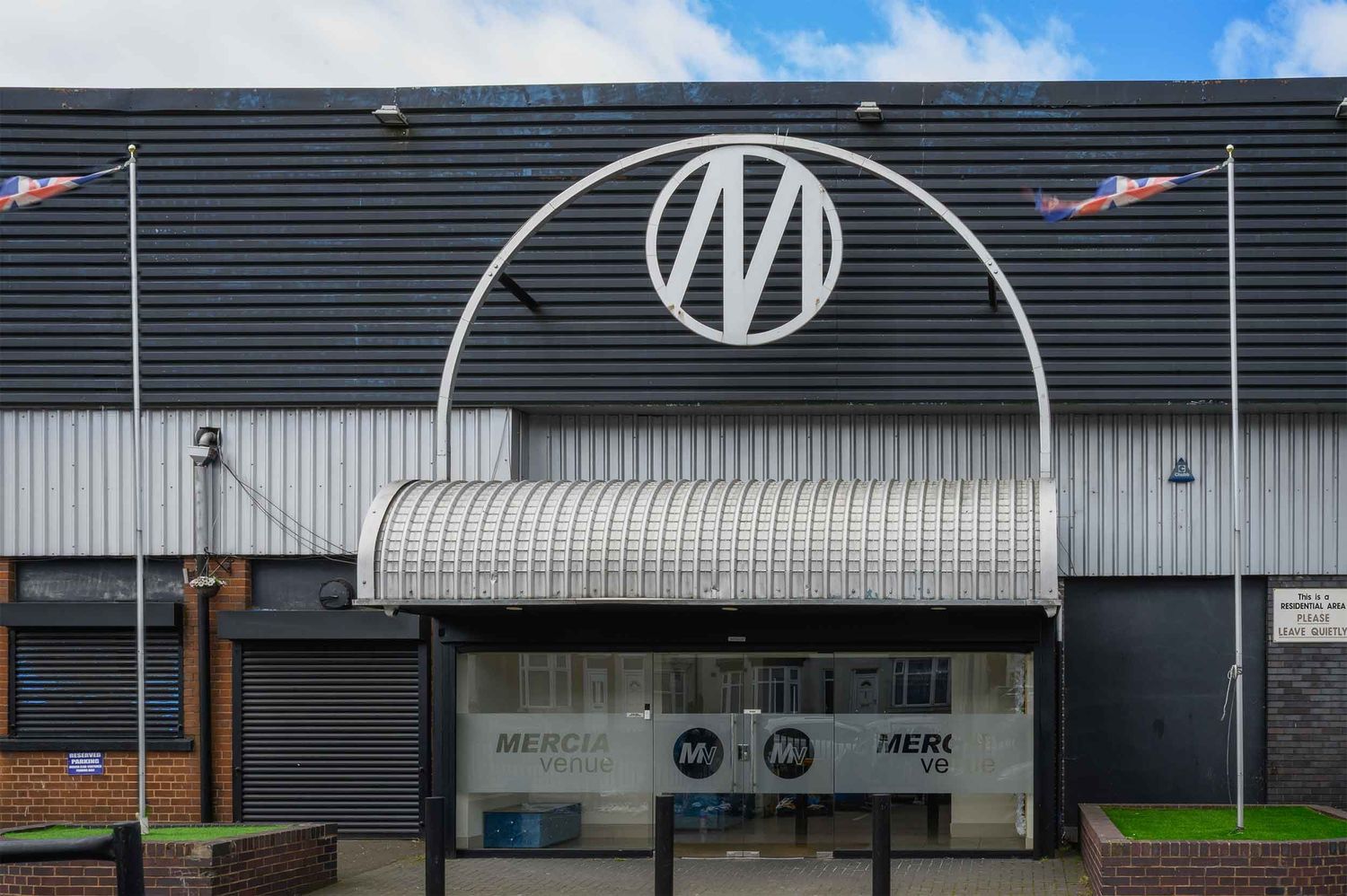 The Mercia Wedding Venue building exterior with a large circular M logo on corrugated metal and a curved entrance.