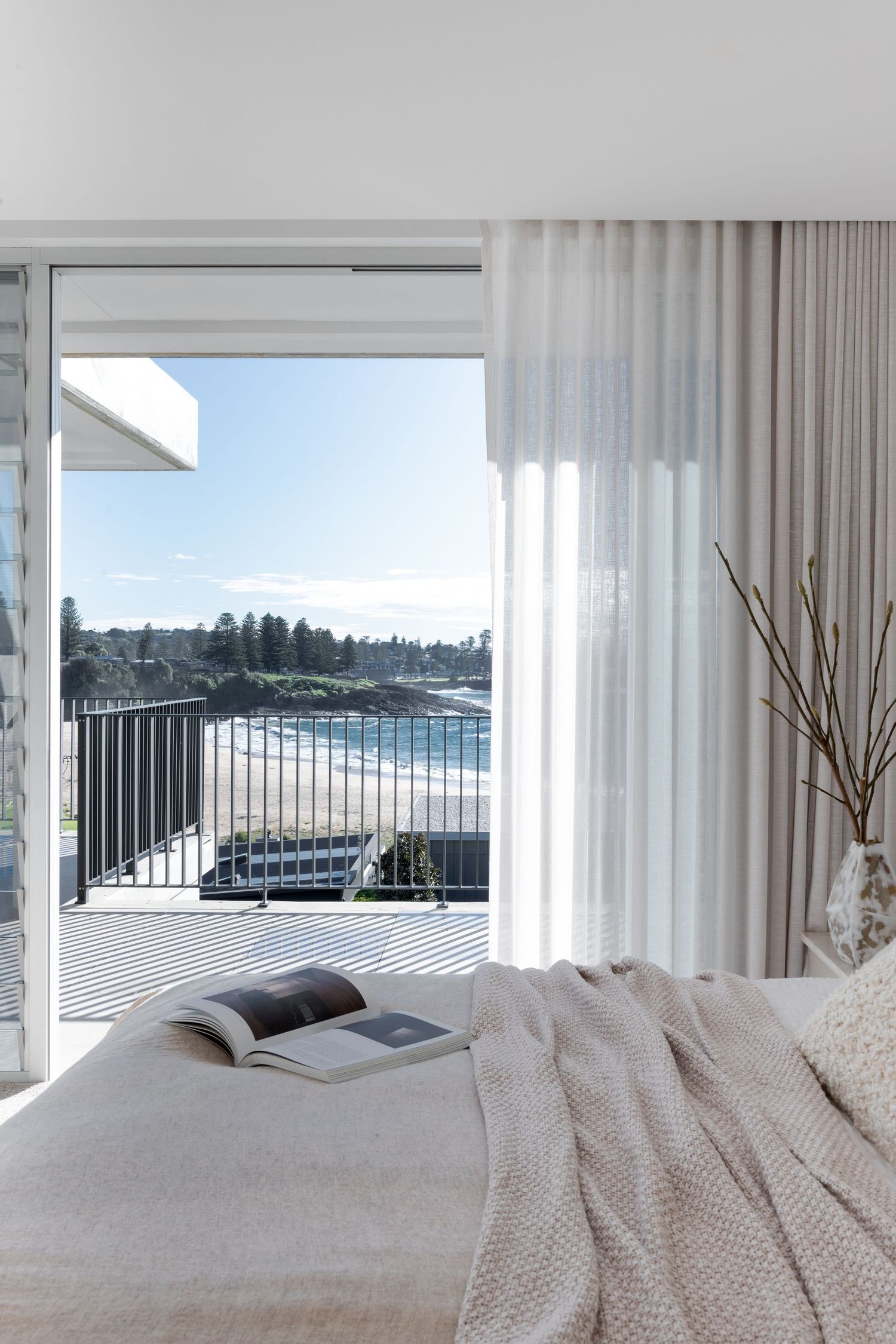 Coastal bedroom with ocean view balcony, white bedding, and sheer curtains.