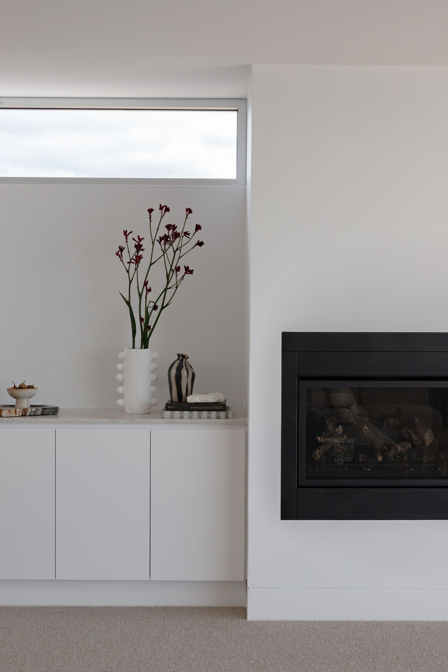 Modern white living room with built-in cabinets, red floral arrangement, and sleek black fireplace insert.