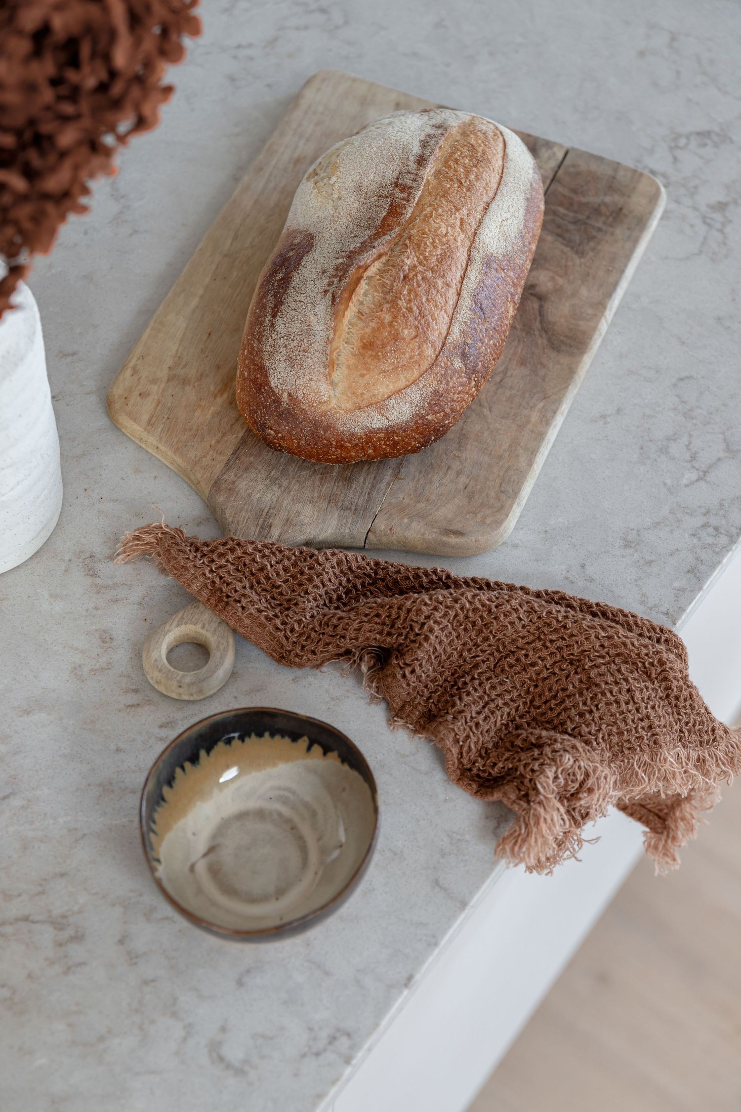 Artisanal sourdough bread loaf on wooden board with brown mesh cloth and ceramic bowl.