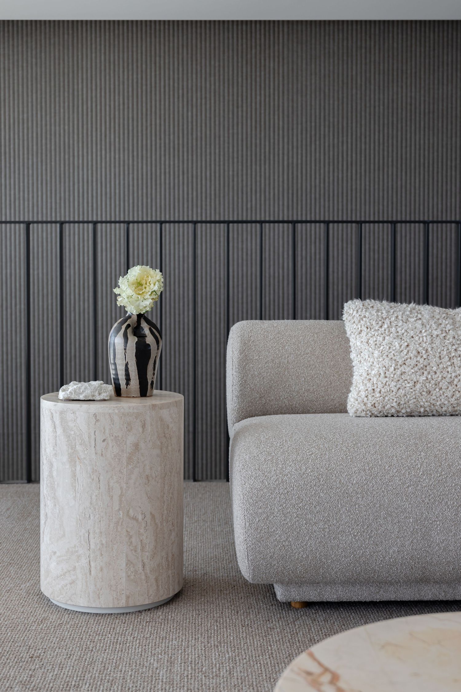 Grey textured wall panel with modern modular sofa and cylindrical concrete side table.