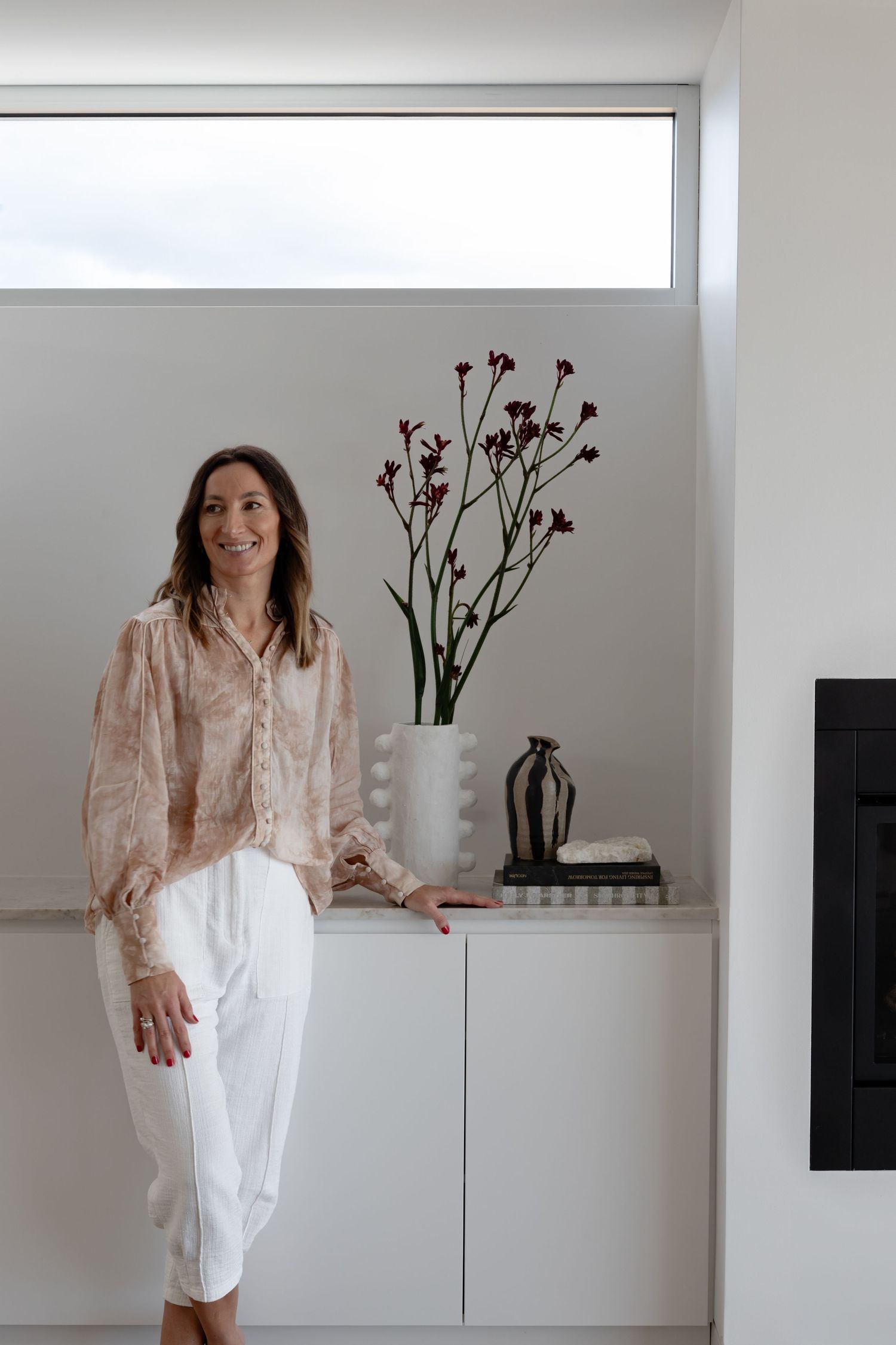 Minimalist interior with white cabinets, red floral arrangement, and black fireplace.