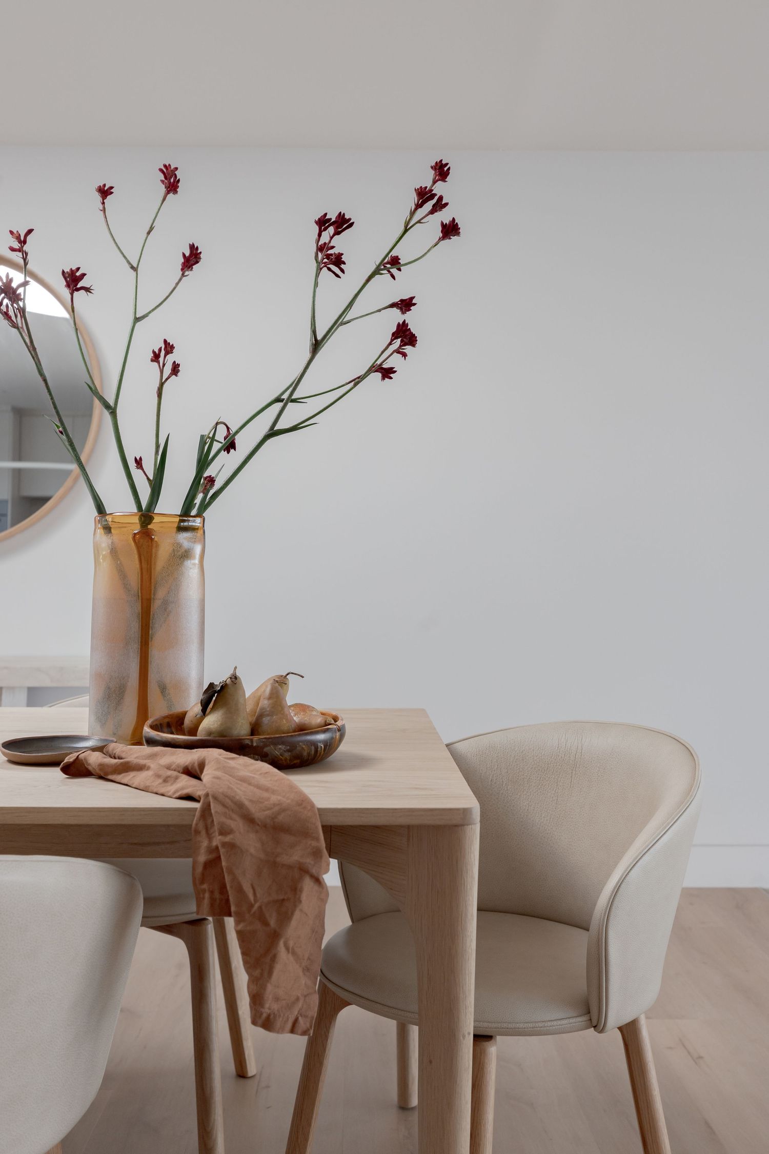 Elegant dining area with beige upholstered chairs and dried floral arrangement on wooden table.