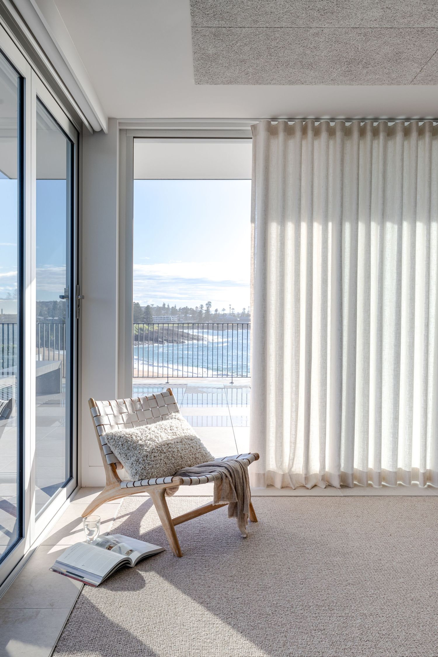 Cozy reading nook with ocean view and modern lounge chair by floor-to-ceiling windows.