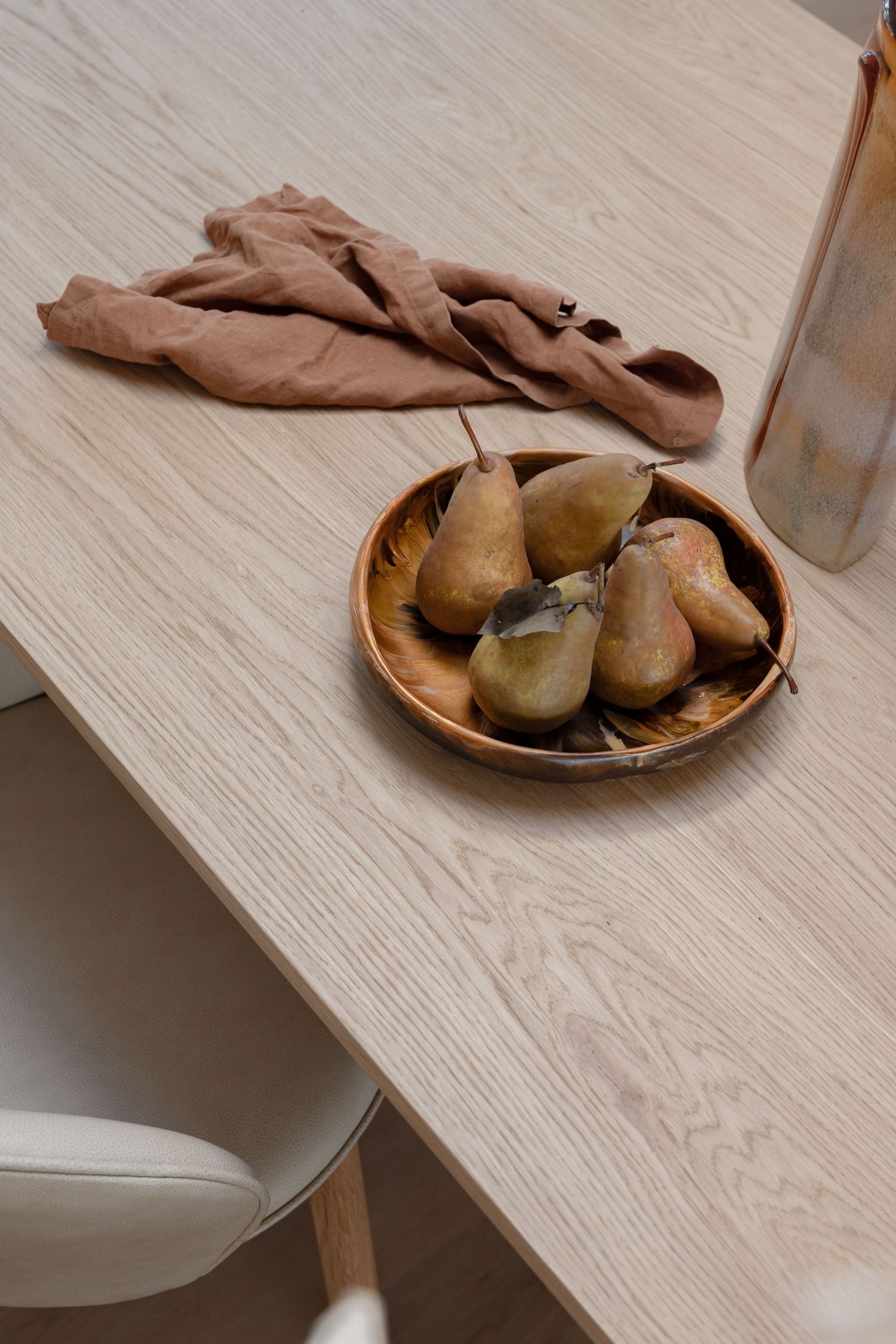 Wooden dining table with pears in ceramic bowl and terracotta linen napkin.