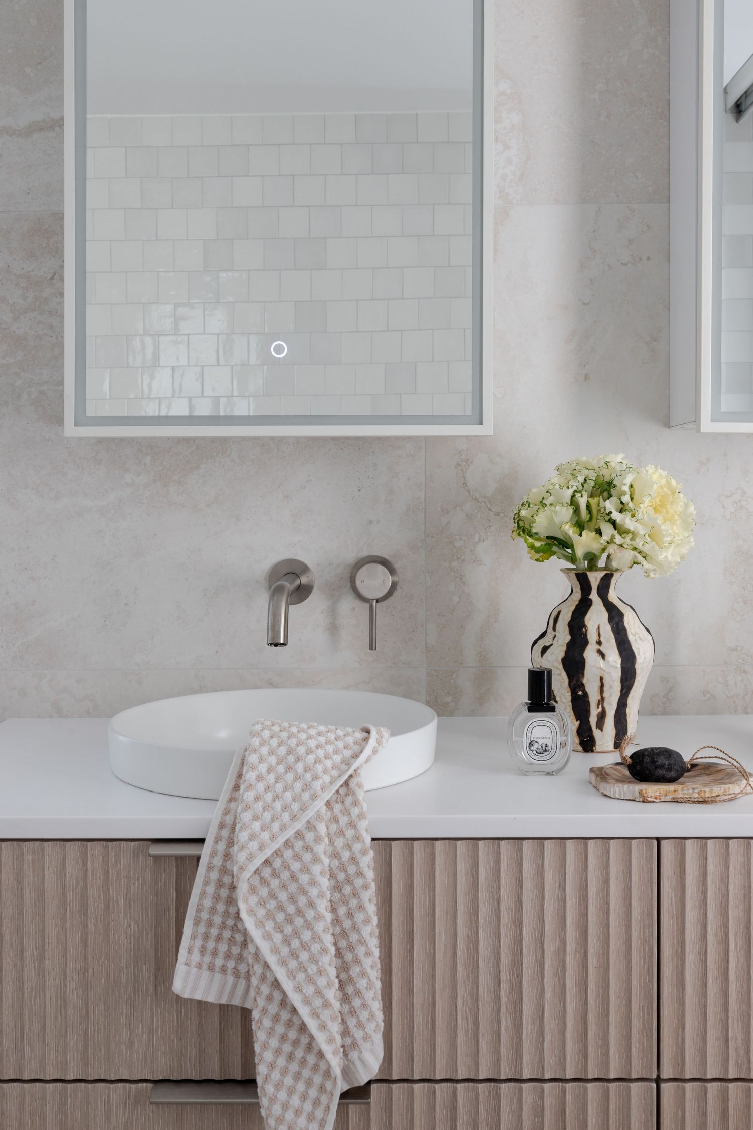 Minimalist bathroom vanity with round vessel sink, wall-mounted faucet and hydrangeas in a glass vase.