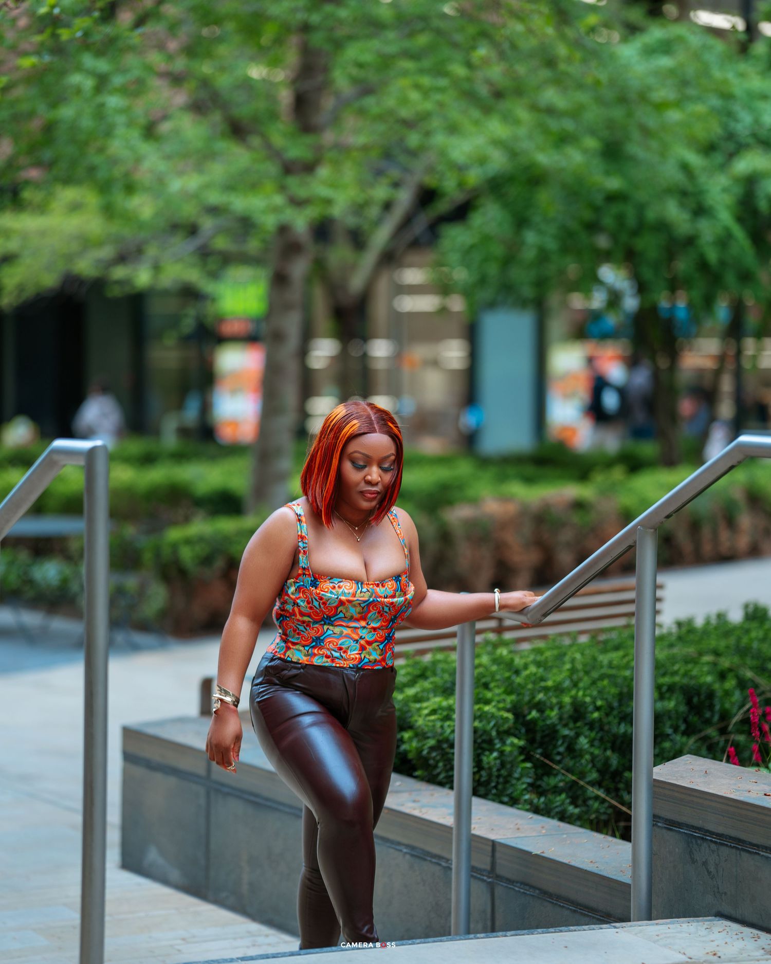 Woman in floral tank top and shiny pants walking up outdoor stairs in an urban garden setting.