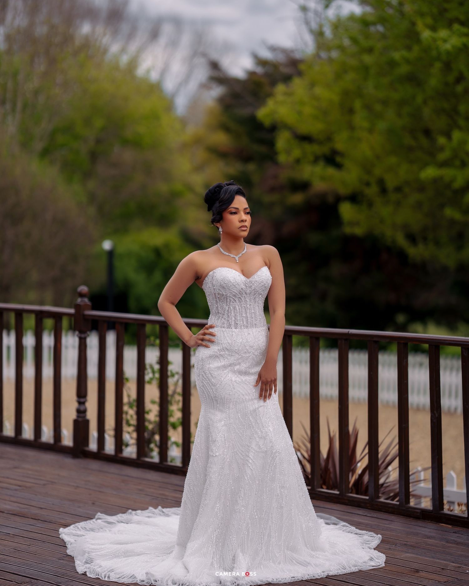 A stunning mermaid style wedding gown with sweetheart neckline and lace details photographed on a wooden deck outdoors.