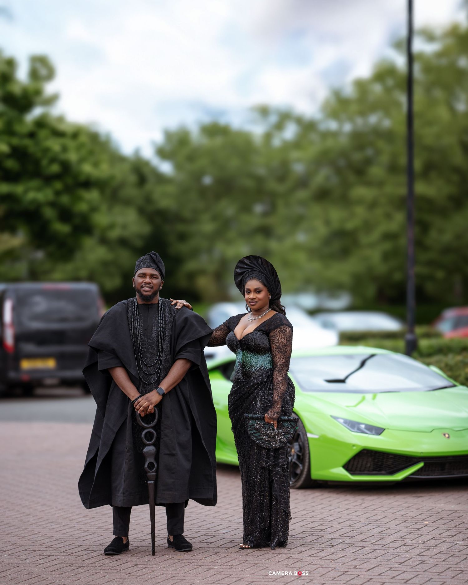 Two people in formal attire pose in front of a bright green Lamborghini sports car parked on cobblestone pavement.