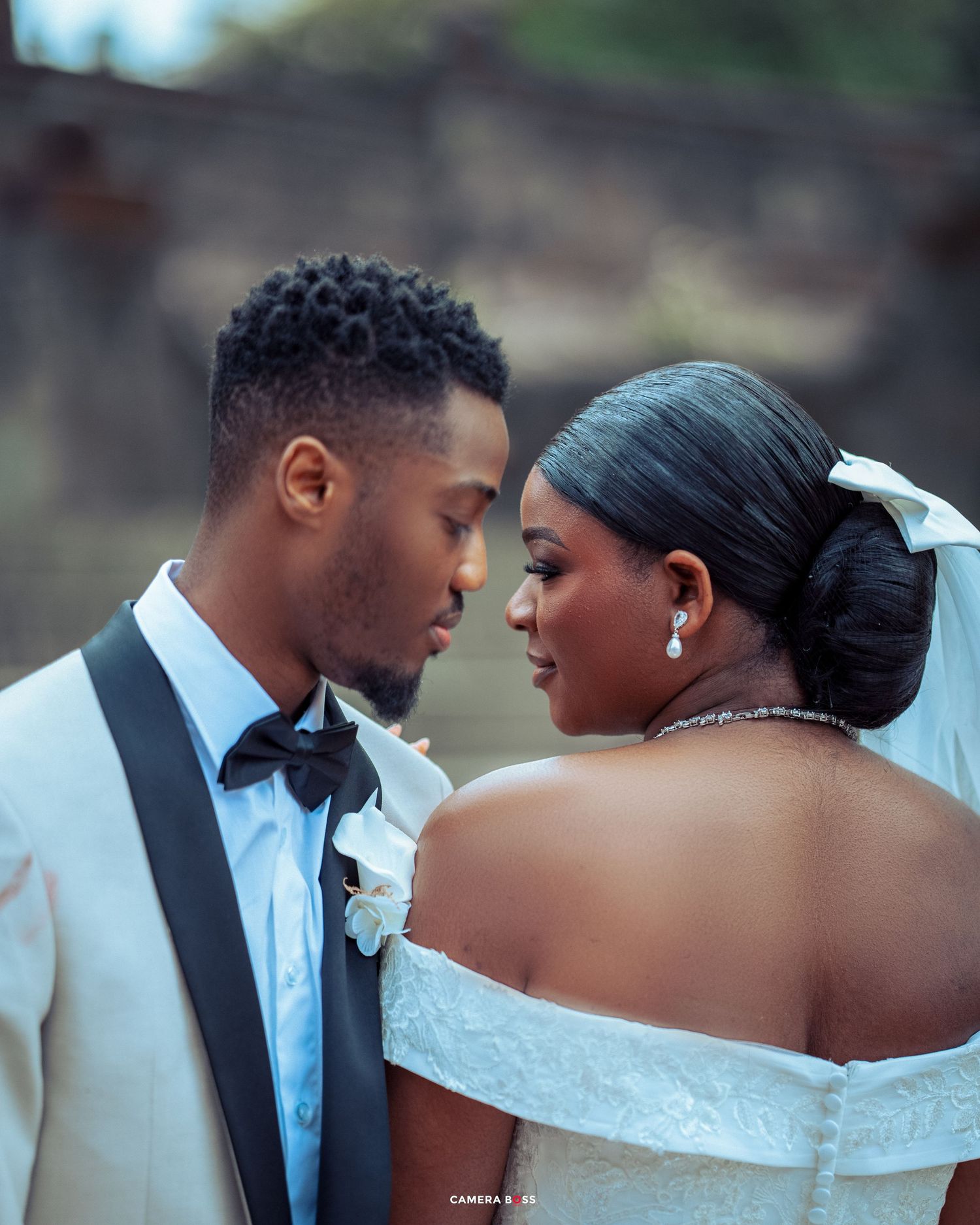 A tender moment between newlyweds at their wedding, with the bride in a white off-shoulder gown and groom in a black tuxedo.