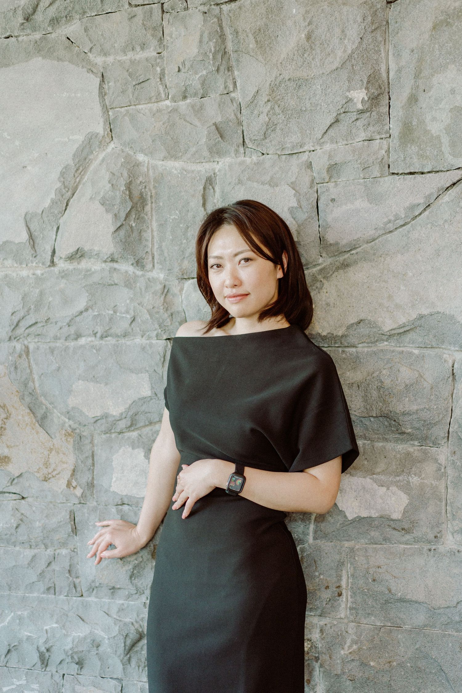 Professional portrait against textured stone wall featuring classic black dress.