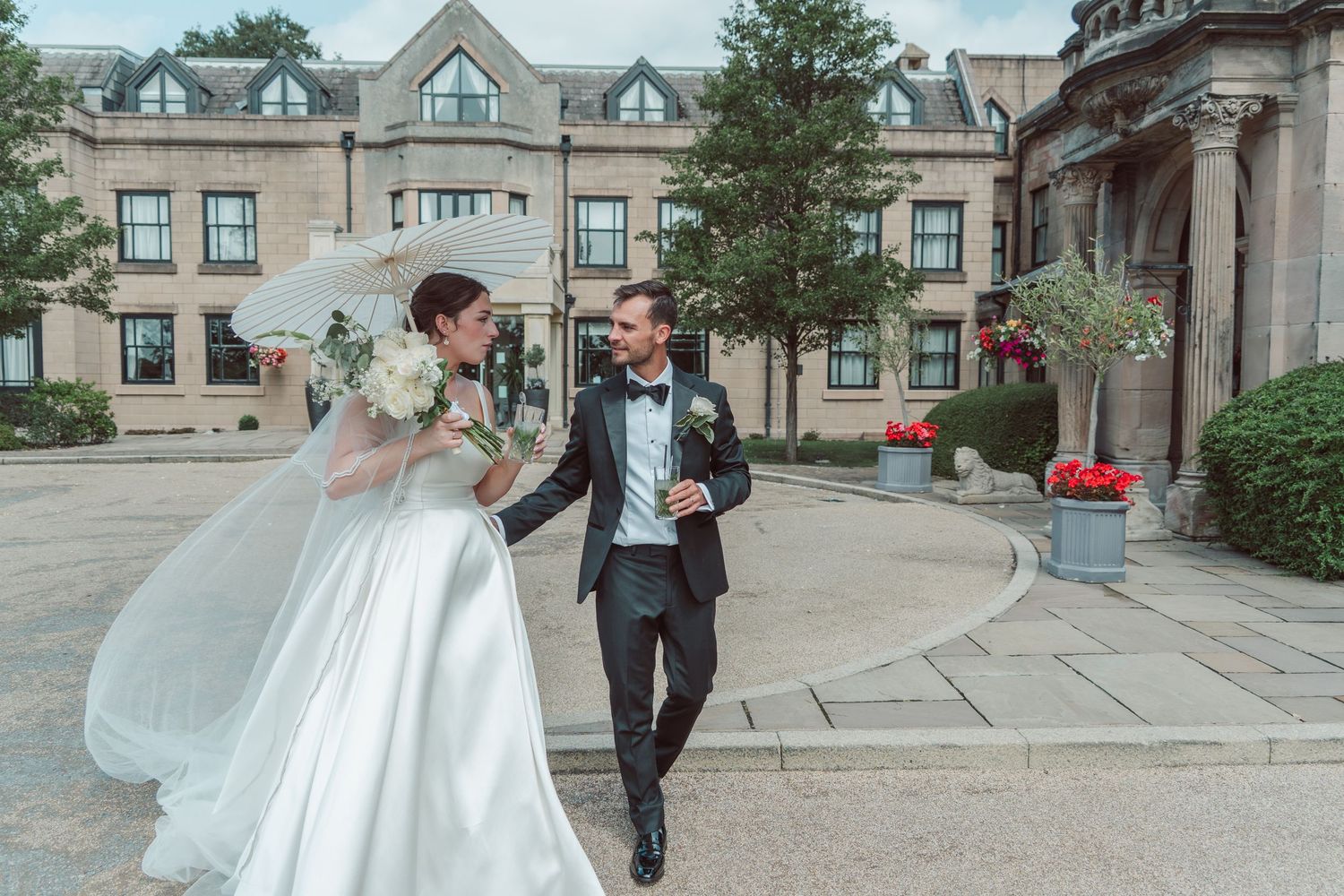 A wedding couple walks together and laughs on the steps of an elegant brick building.