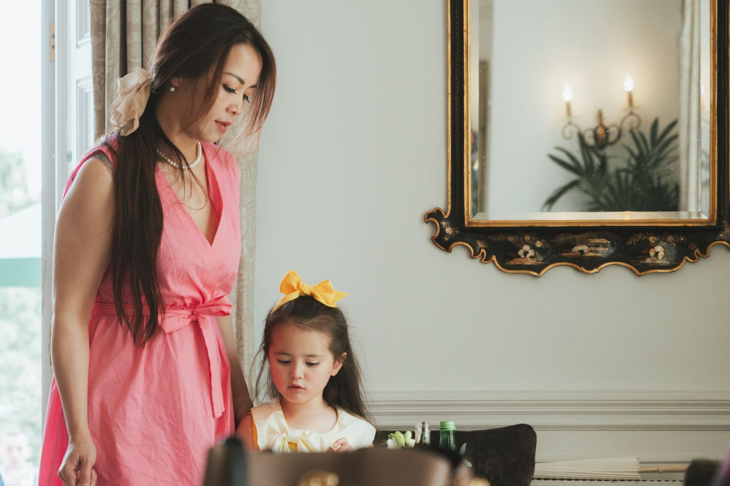 Mother and daughter in pink dresses at piano in elegant room.