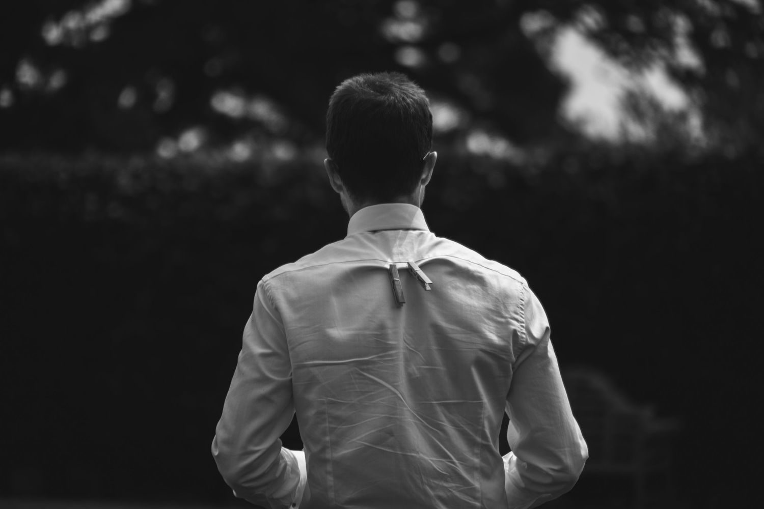 Back view of person in white button-down shirt standing against dark background in black and white photo.