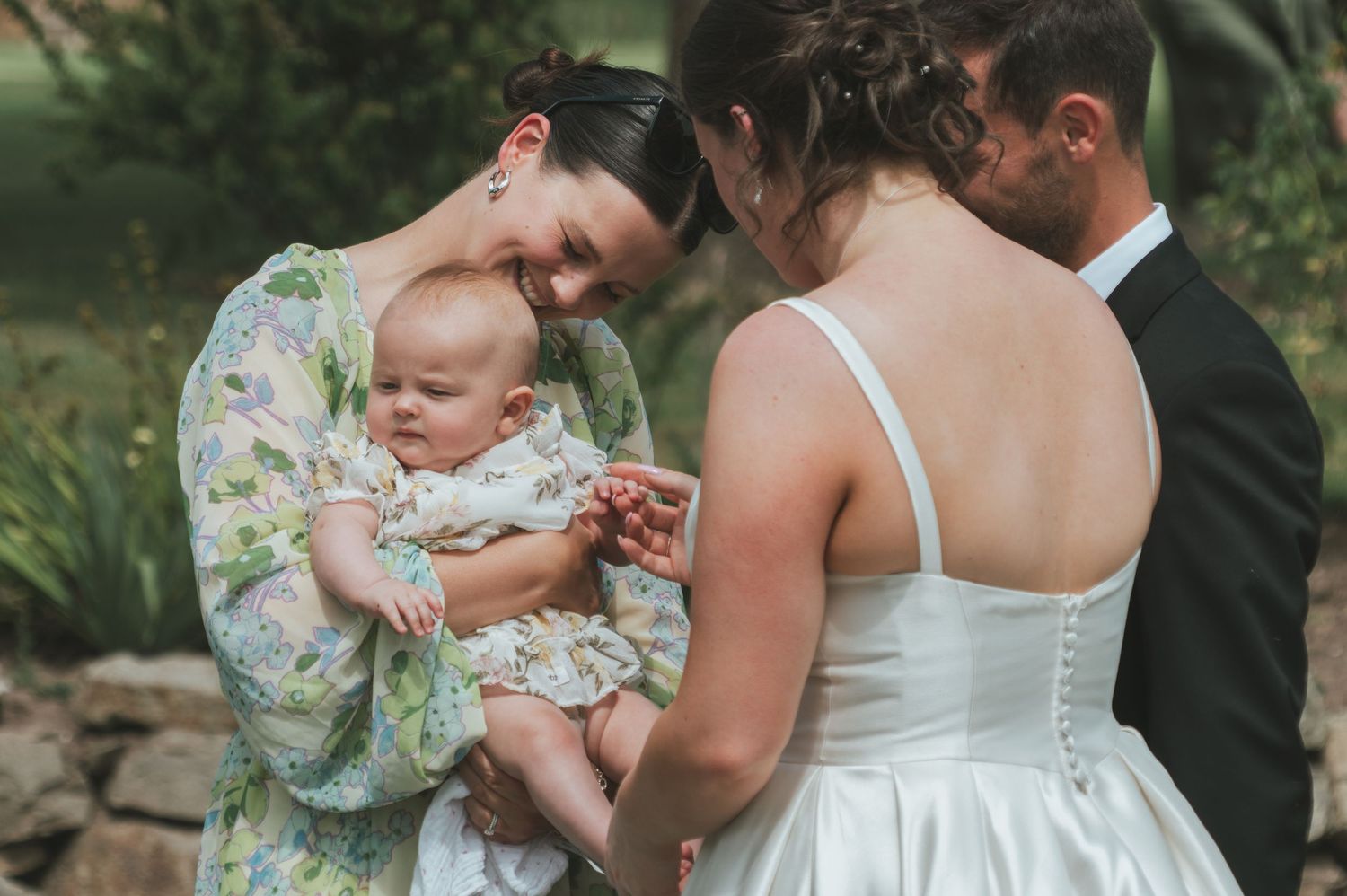Wedding guests gather around a small baby during an outdoor reception.
