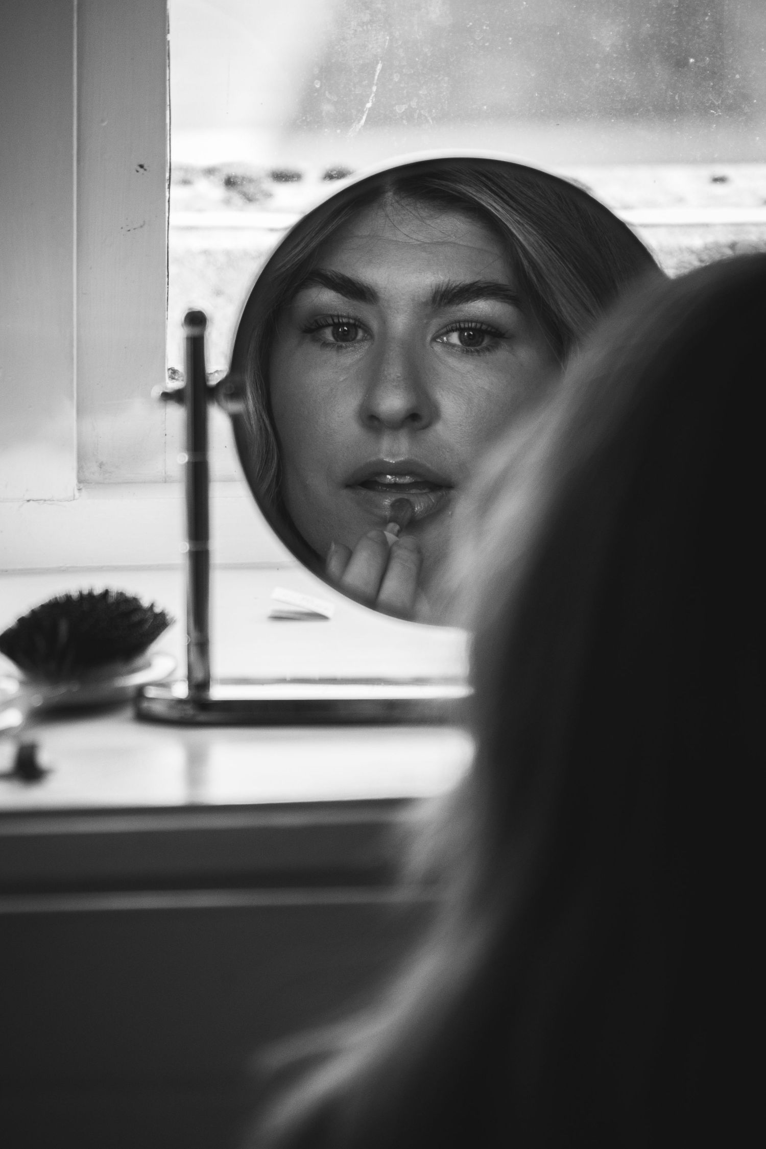 Black and white reflection of person applying lipstick in vanity mirror.
