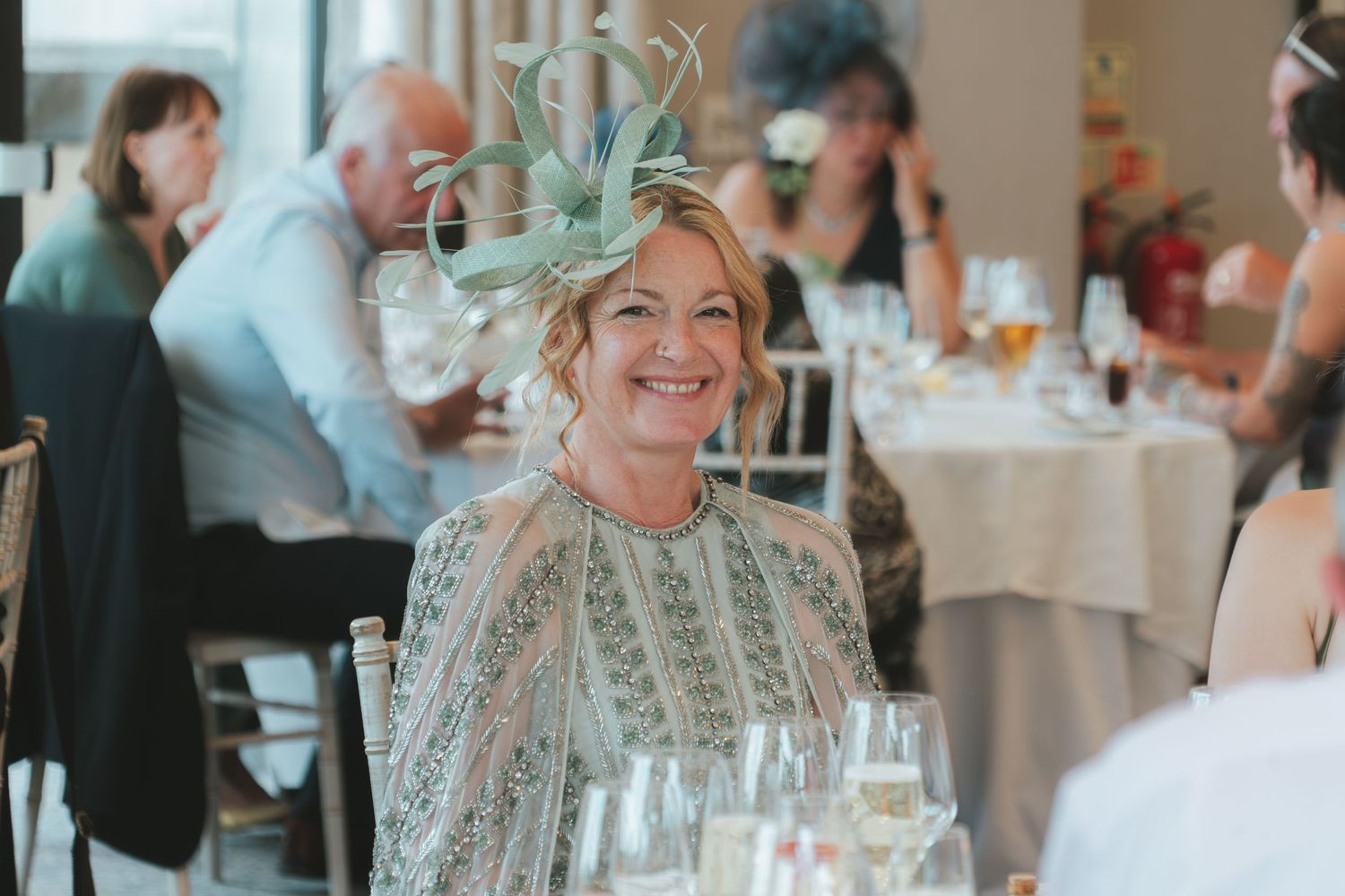 Wedding guest in mint green dress with fascinator enjoying reception dinner.