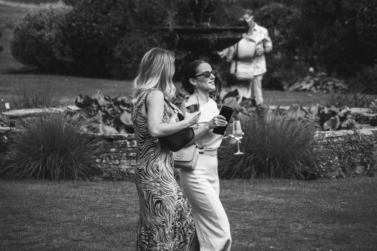 Wedding attendees dancing together in a garden setting captured in black and white.