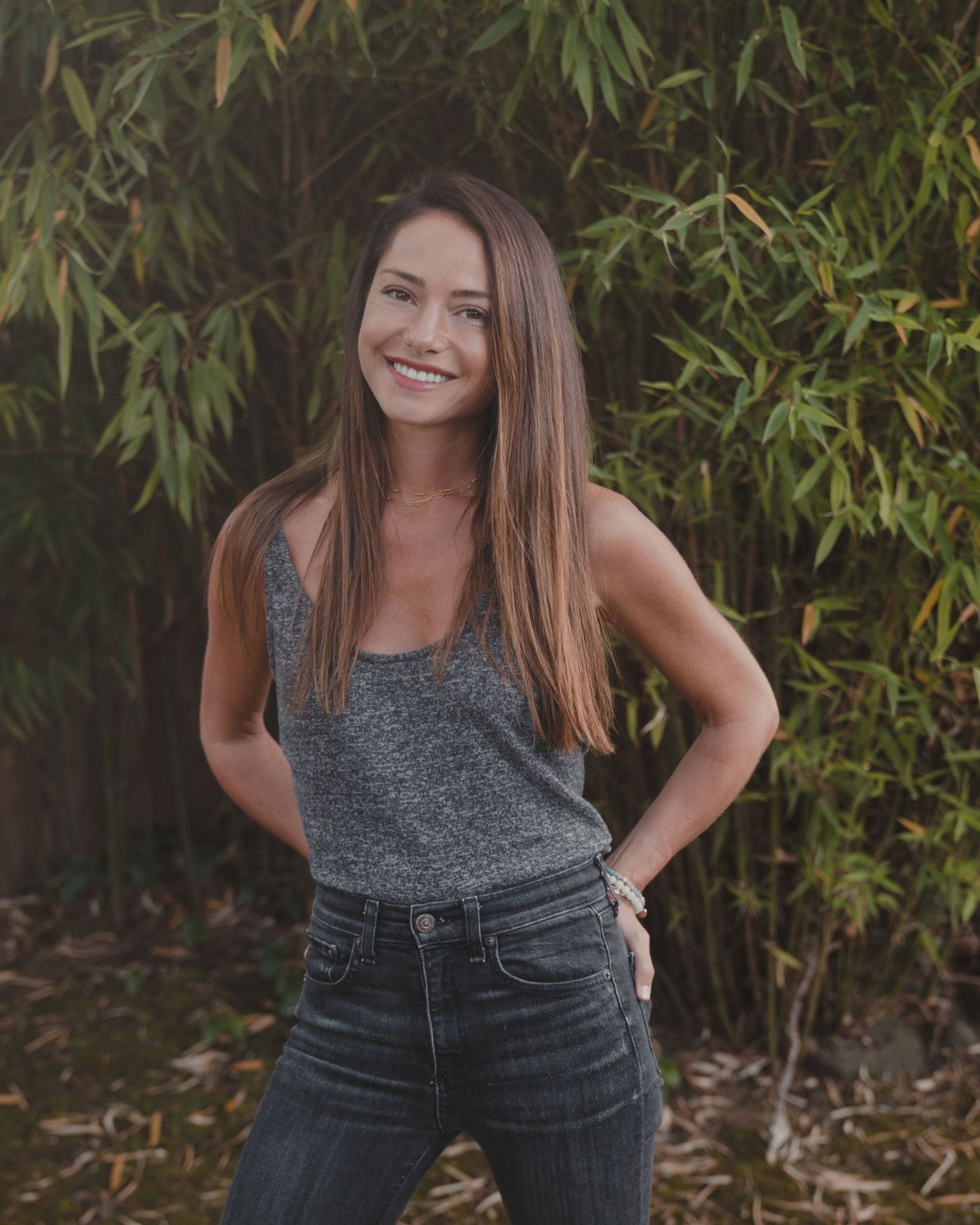 Casual portrait against bamboo backdrop with relaxed pose in tank top and jeans.