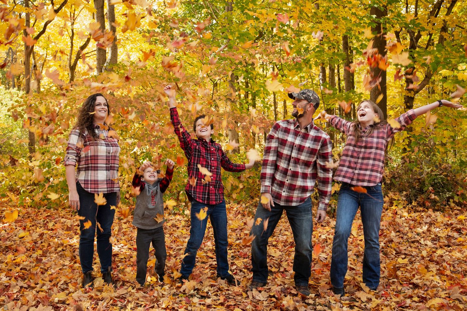 Family photography session with coordinated plaid outfits against fall foliage backdrop.