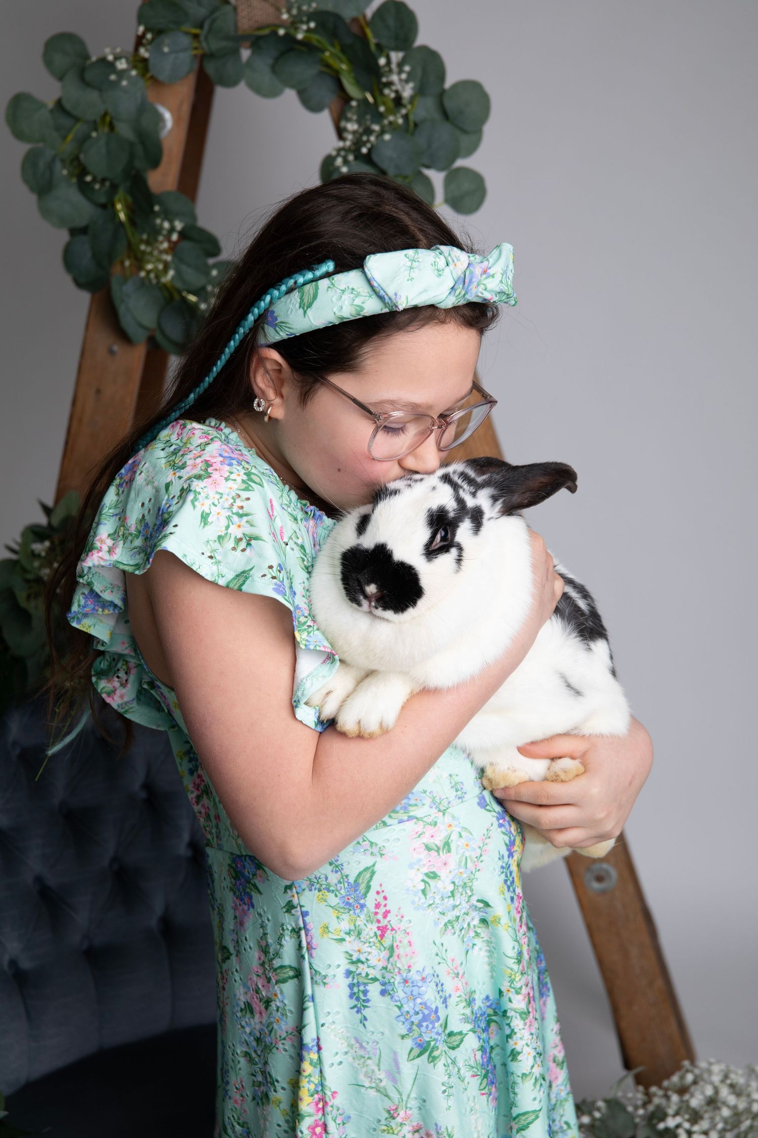 Young person in mint floral dress holding black and white rabbit during portrait session.