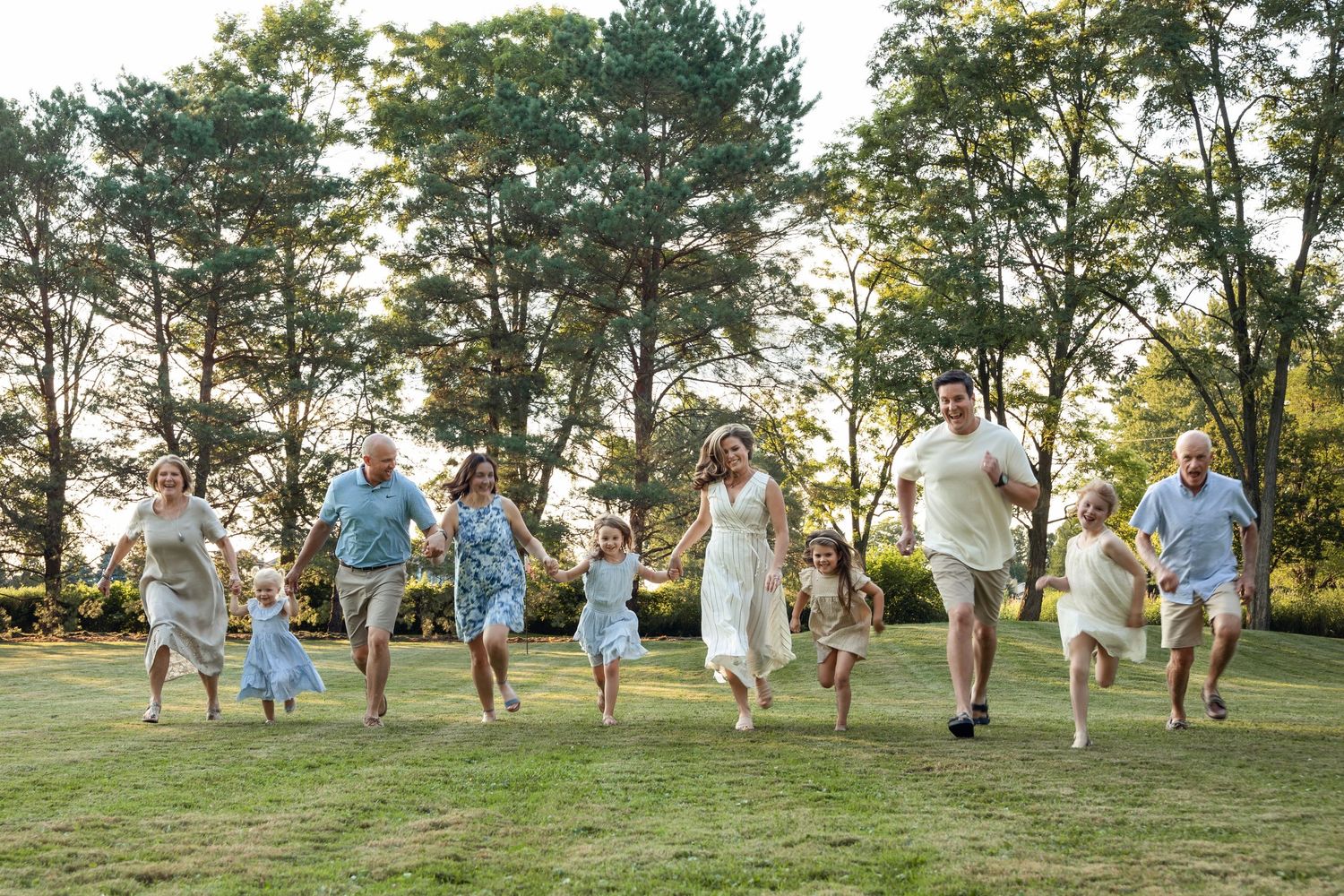 Extended family group running and jumping together on grassy hill during golden hour.