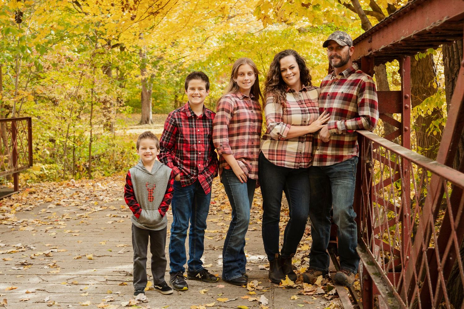 A family group portrait on rustic bridge surrounded by golden autumn trees.