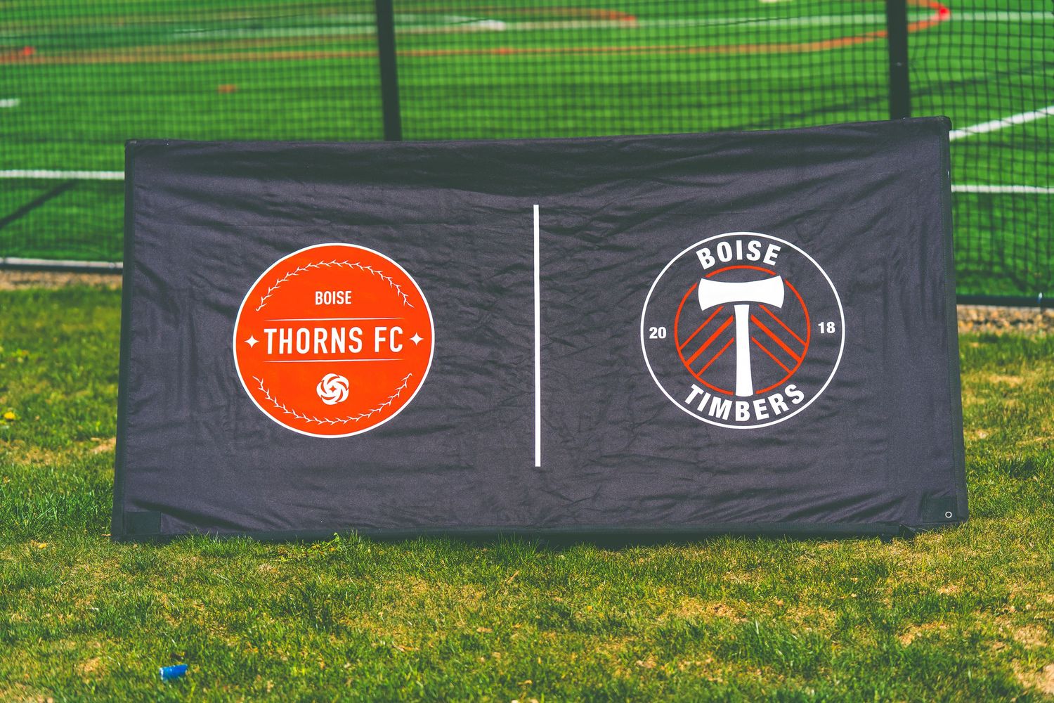 A grey banner displaying two soccer team logos - Thorns FC and another circular emblem on a grass field.