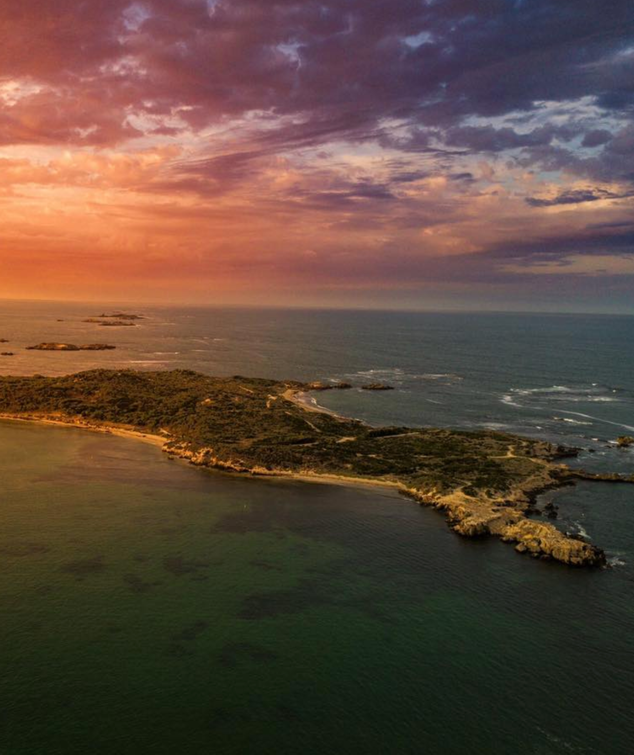 Aerial view of rocky coastline during golden sunset with dramatic clouds over ocean.