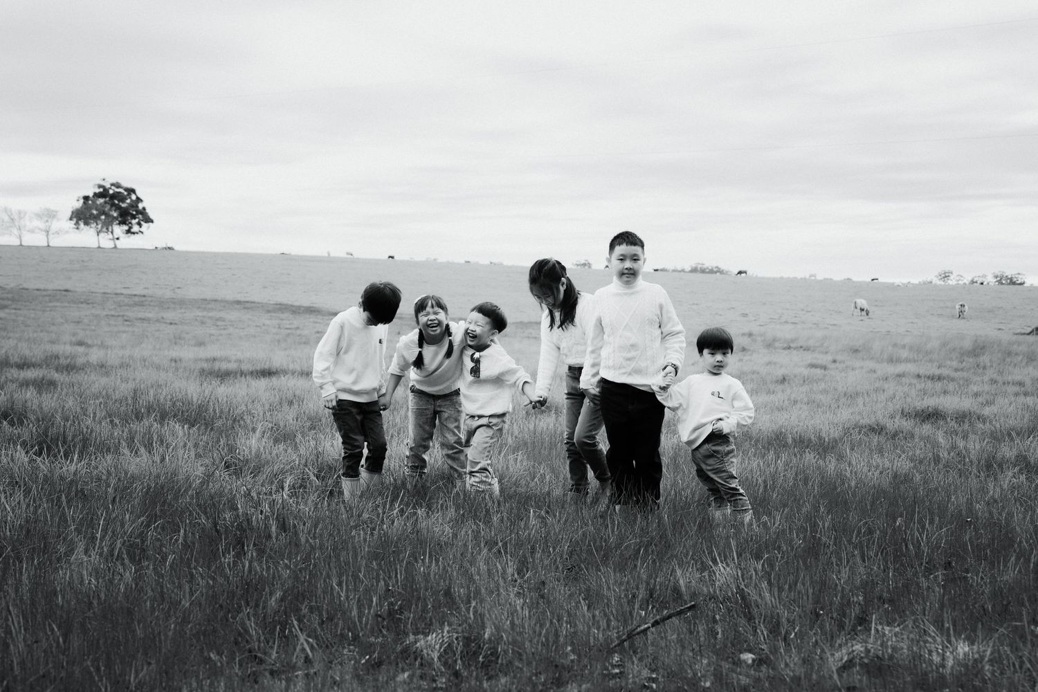 Group running together through tall grass field in black and white photograph.