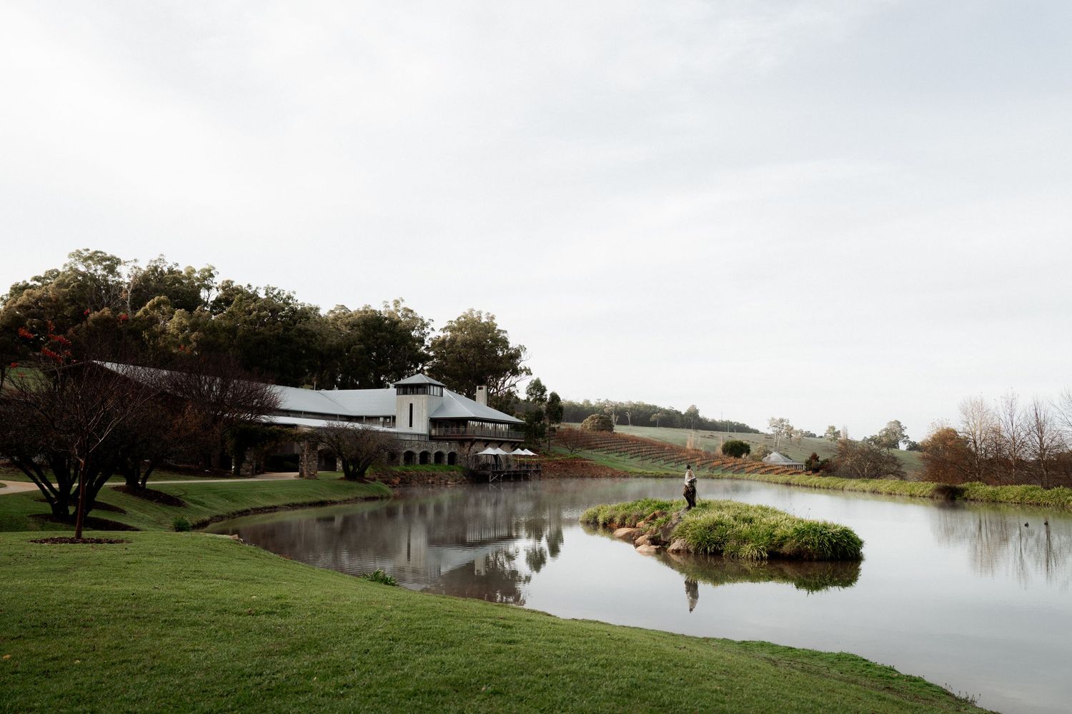 Millbrook Winery reflected in a serene pond surrounded by manicured lawns and landscaping on an overcast day.